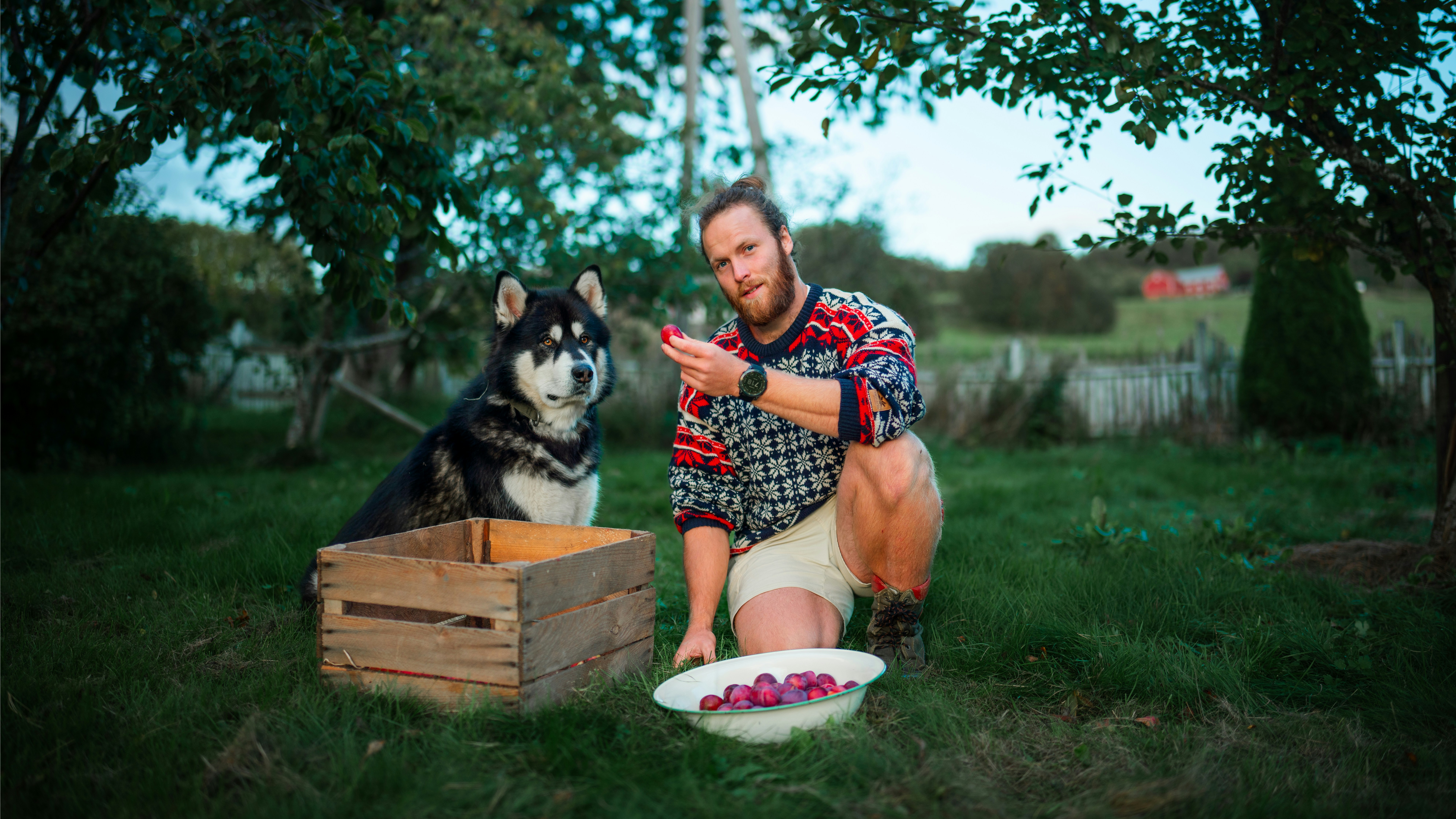 A man kneeling down next to a dog eating out of a bowl