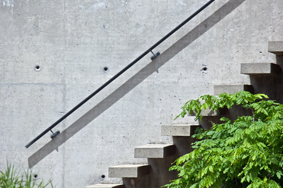Concrete staircase with black metal railing leads up to an unseen destination in gray concrete