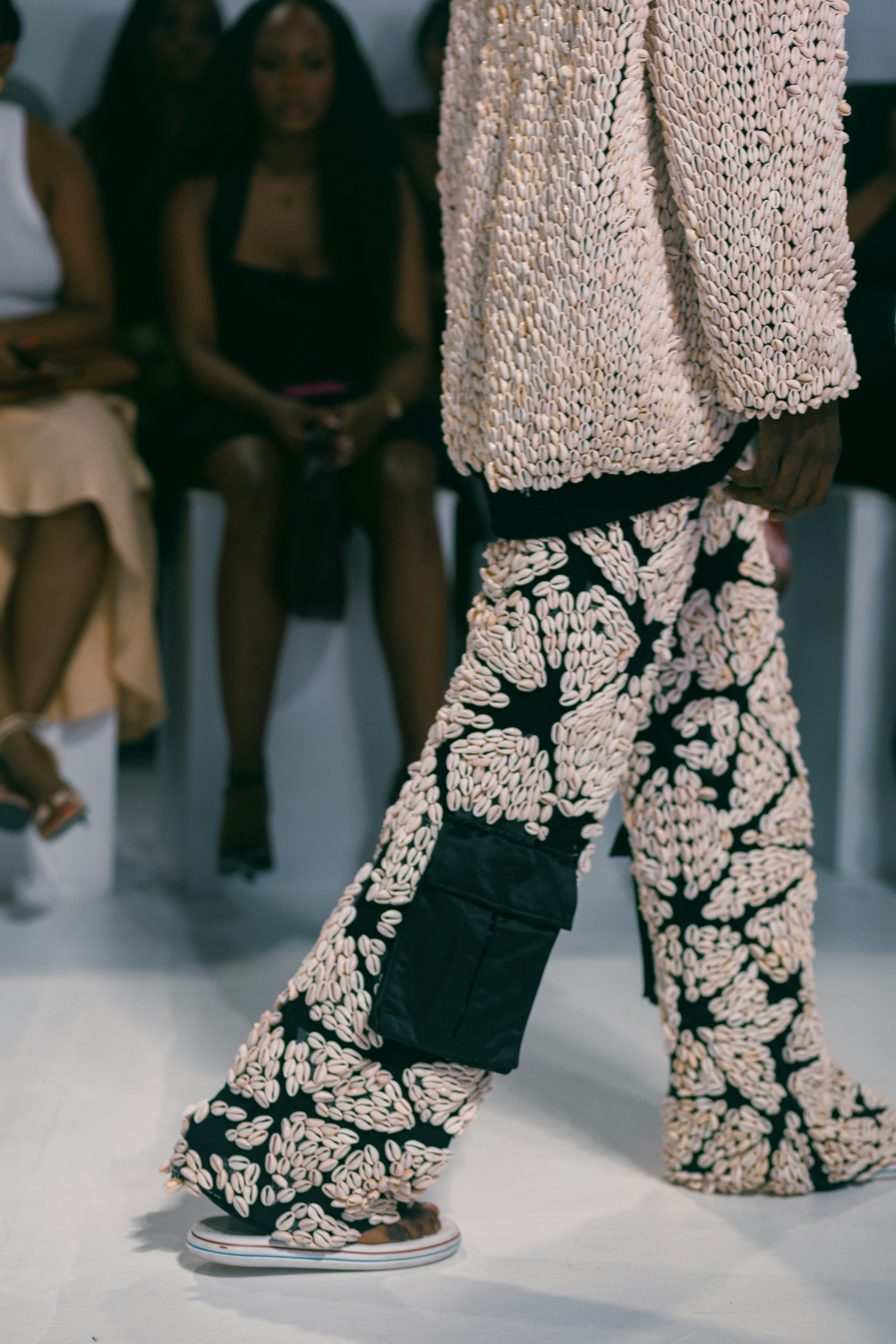 Model walks down a runway wearing an outfit covered in shells.