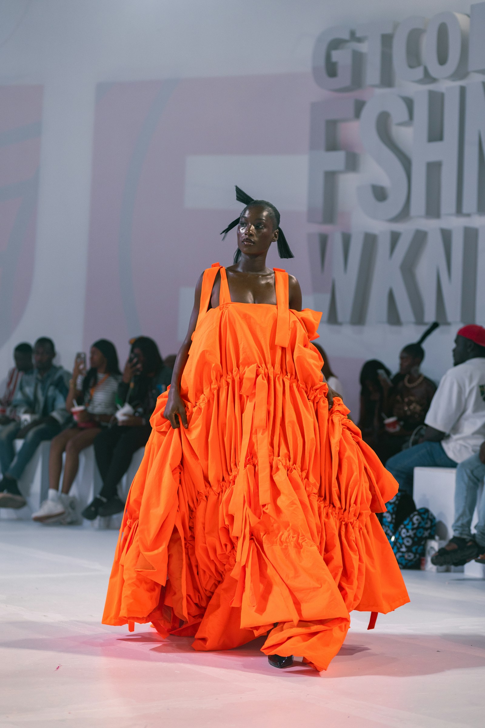 Modelo de vestido laranja volumoso desfilando na passarela