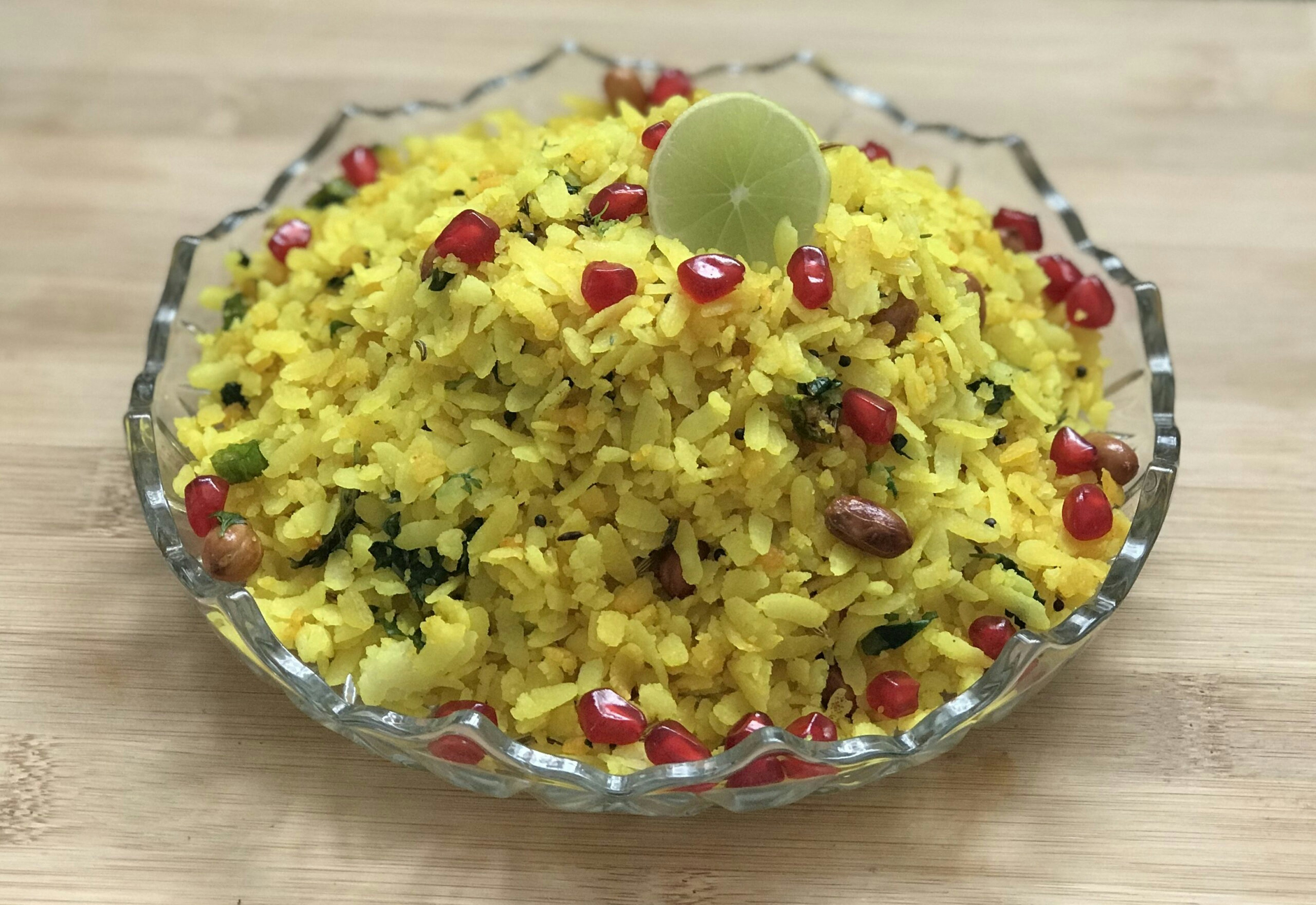 Yellow poha dish garnished with coriander and lemon on a dark background