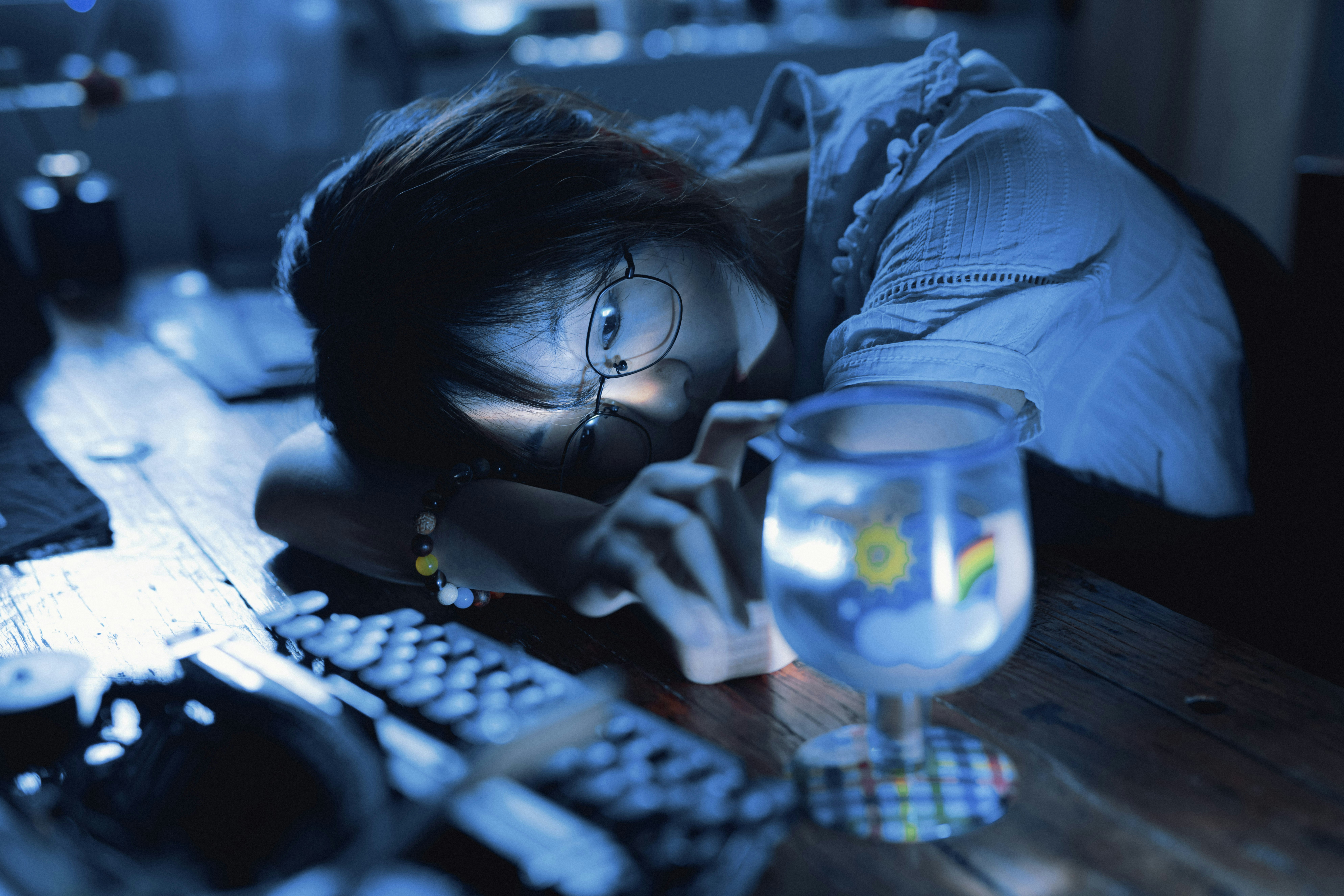 A woman laying her head on a desk next to a computer