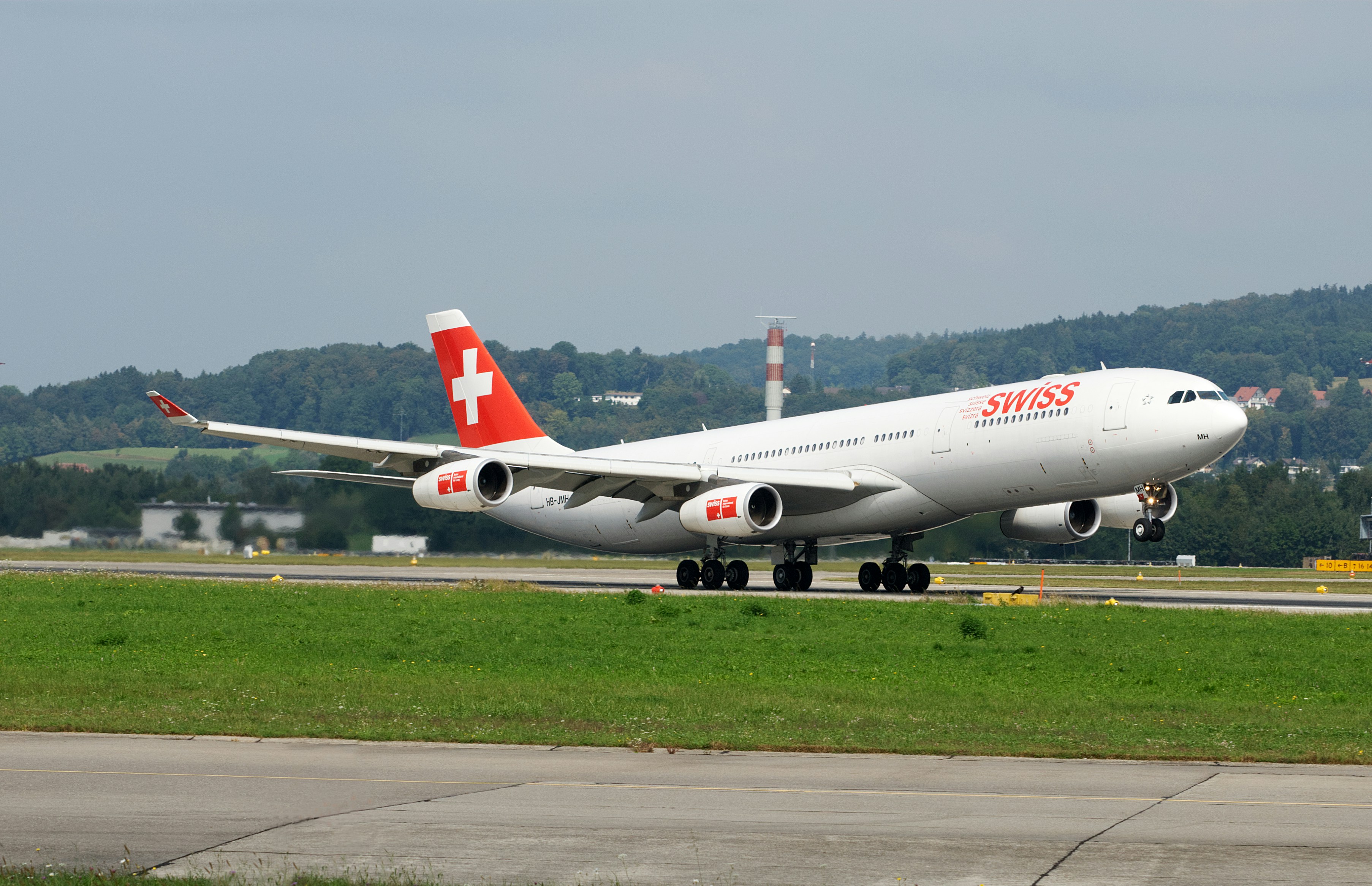 A large jetliner sitting on top of an airport runway, An Airbus A340 passenger plane takes off from Zurich Airport