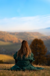 A woman in a green coat sitting on a hill