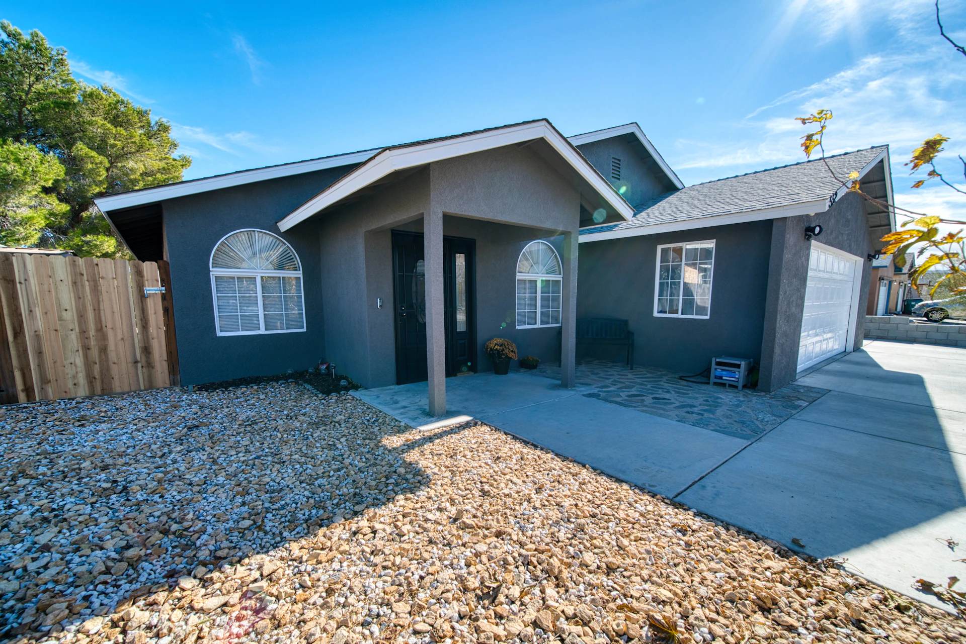 A gray house with a fence and gravel in front of it