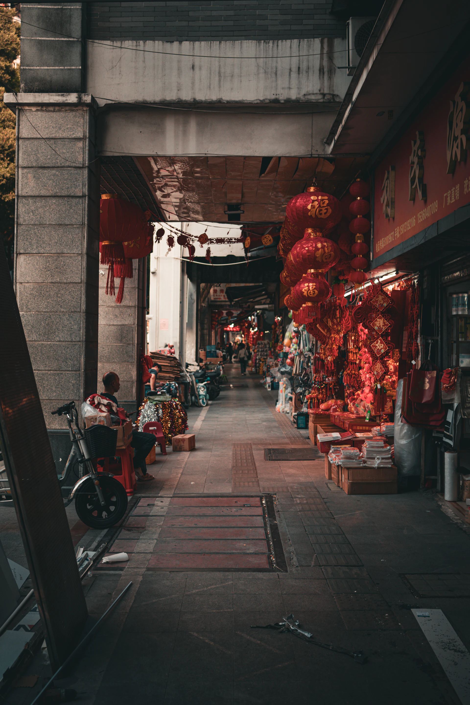 A narrow street with a bunch of red lanterns hanging from the ceiling