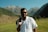 A man standing in a field with mountains in the background