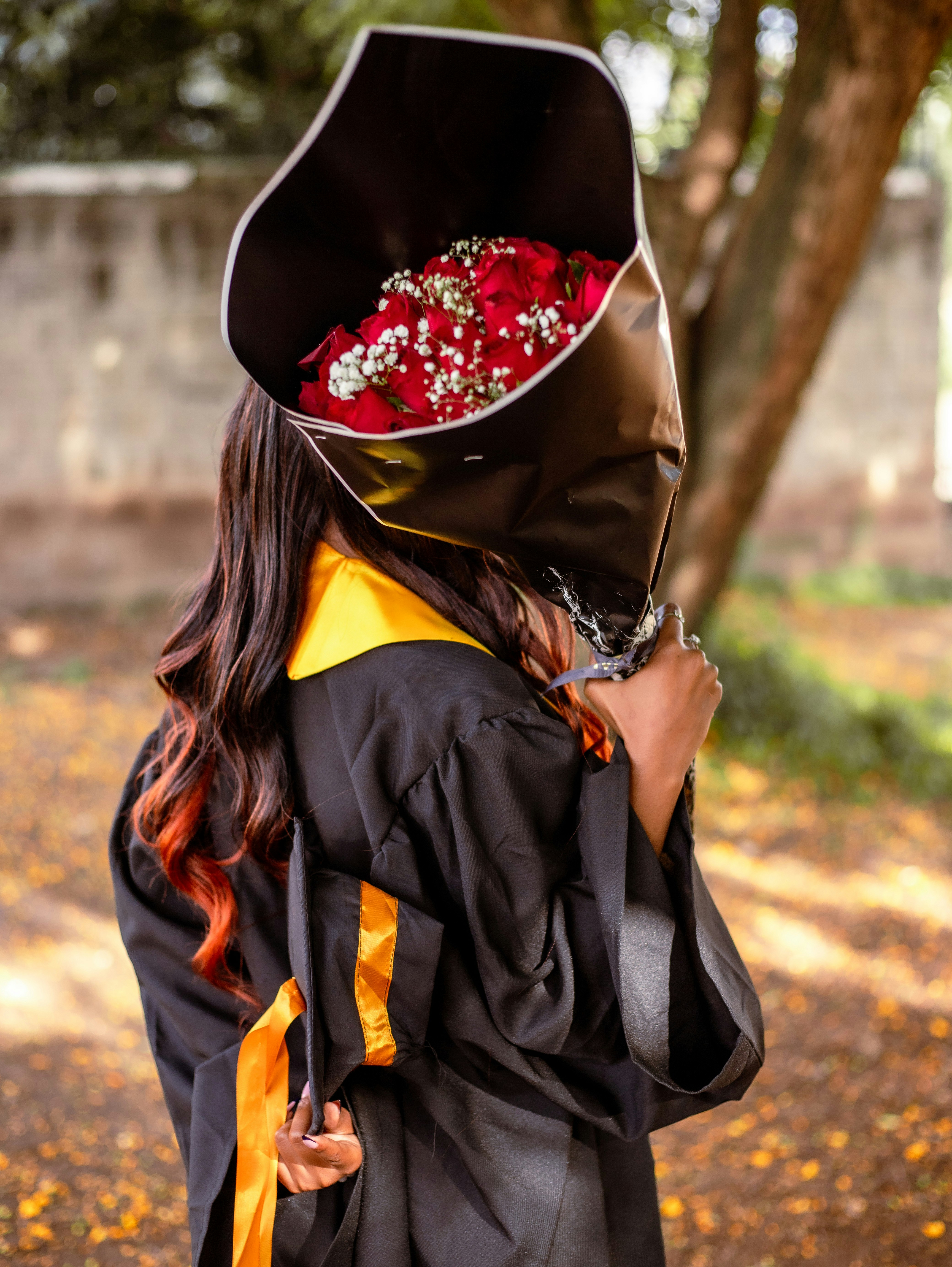 Seorang wanita mengenakan gaun kelulusan dan topi dengan bunga di atasnya