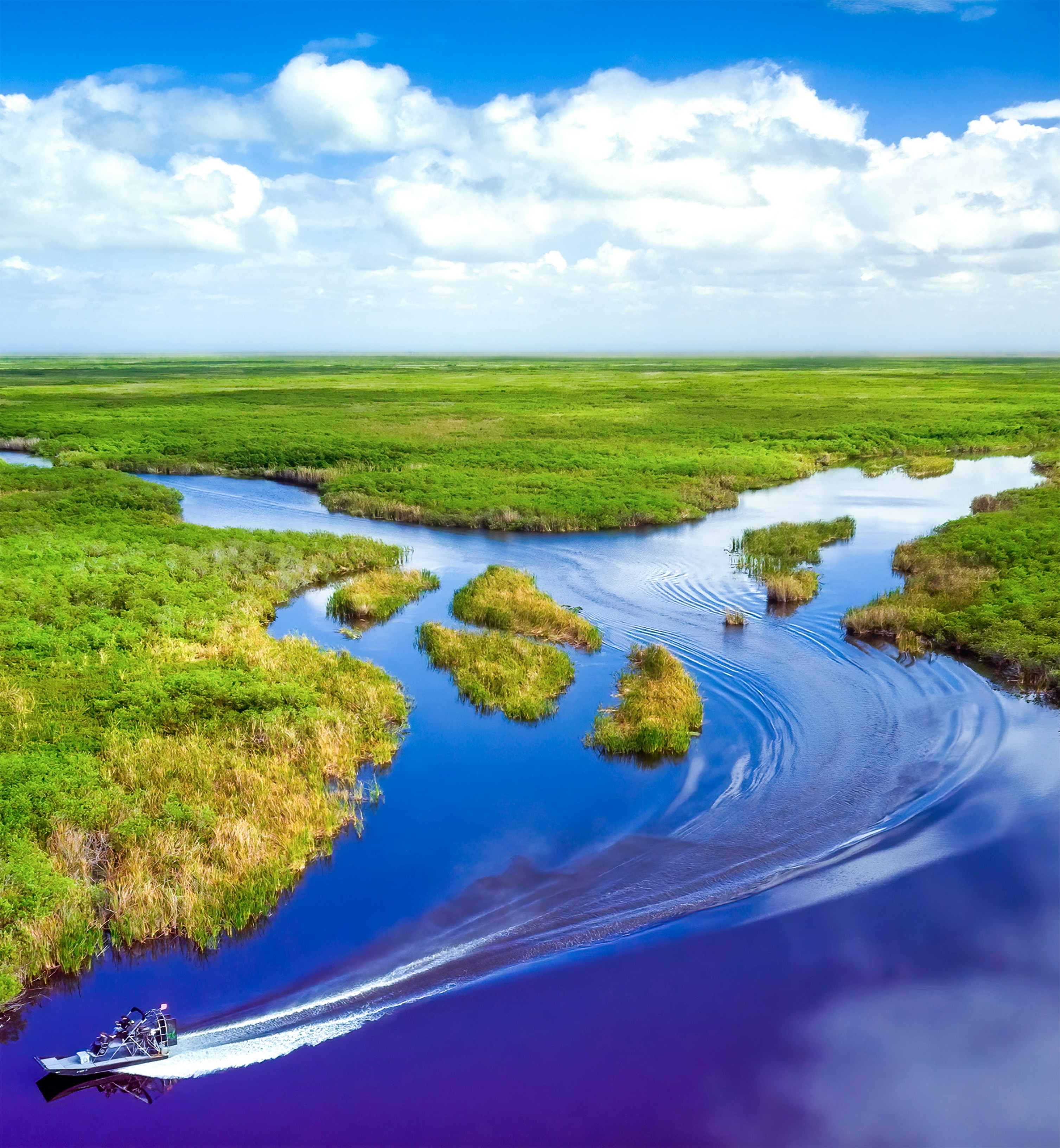 A boat traveling down a river surrounded by lush green fields