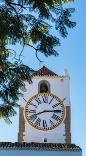 A white clock tower with a yellow and black clock