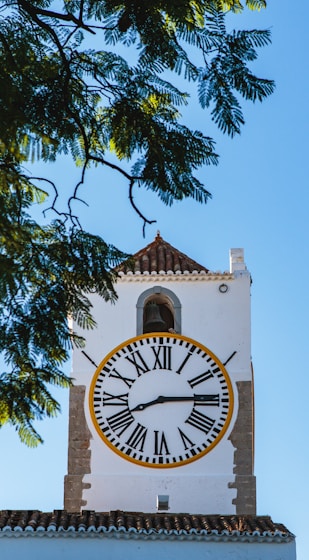 A white clock tower with a yellow and black clock