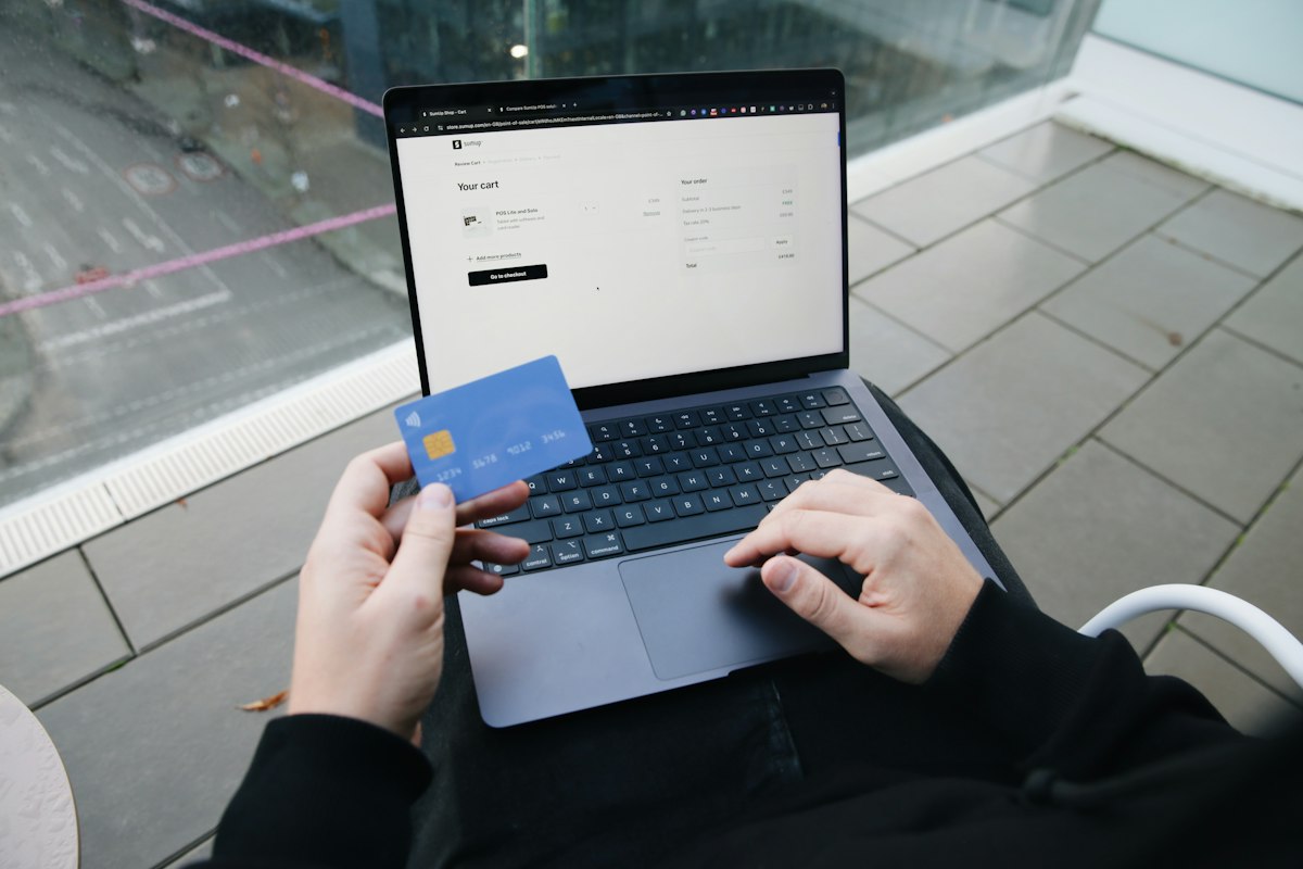 Personne assise devant un ordinateur portable ouvert sur une page de paiement, une carte bancaire bleue à la main