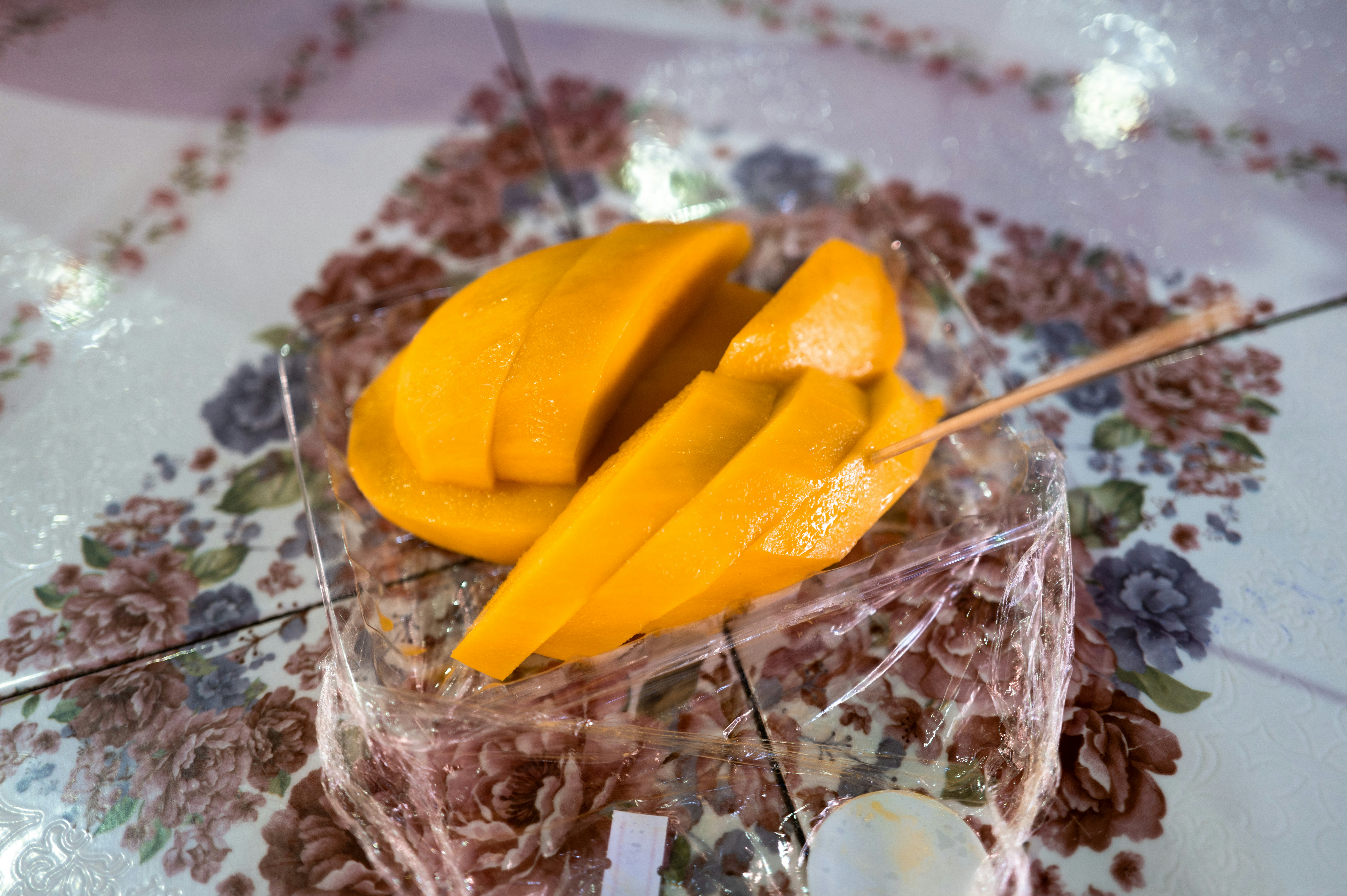Golden ripe mango slices neatly arranged in a white takeout box with lime wedge
