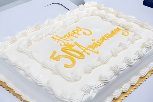 A square white cake with gold lettering on it