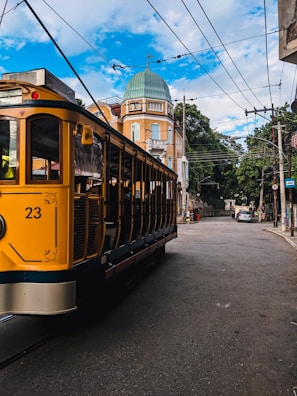 A yellow train traveling down a street next to tall buildings