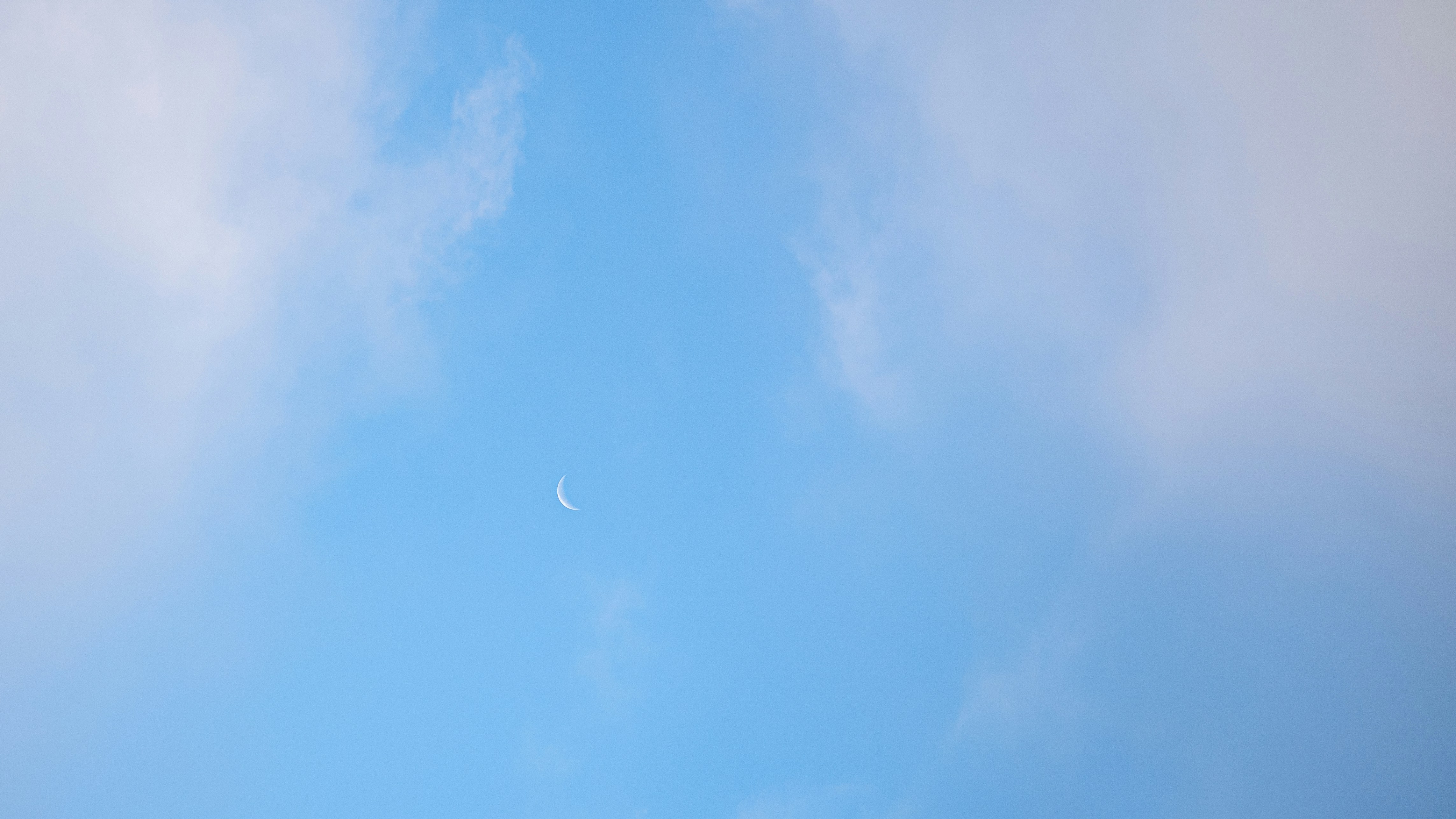 A blue sky with clouds and a half moon