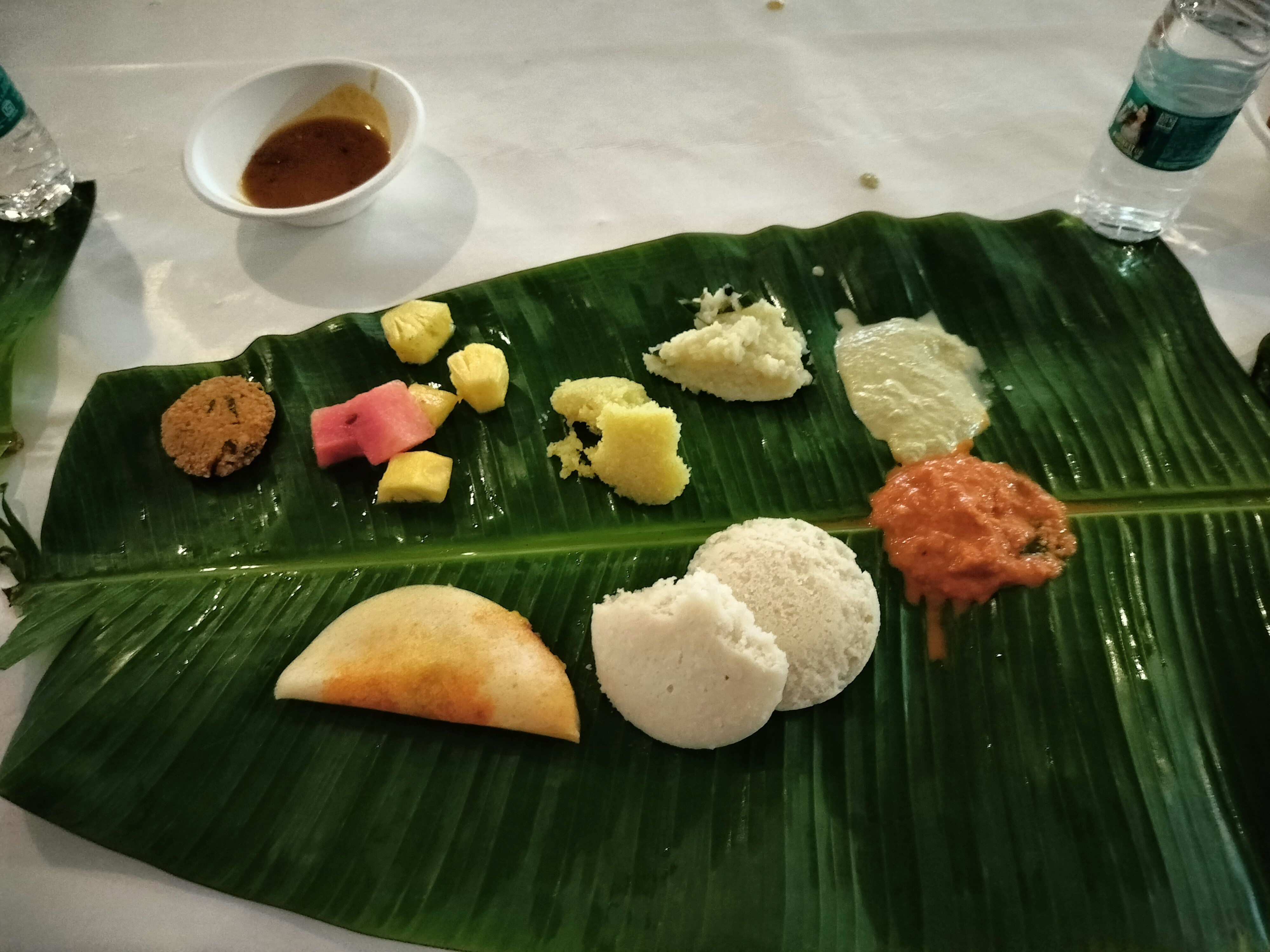 South Indian breakfast spread with masala dosa, sambar bowls and coconut chutney on banana leaf, bright airy restaurant, natural morning light