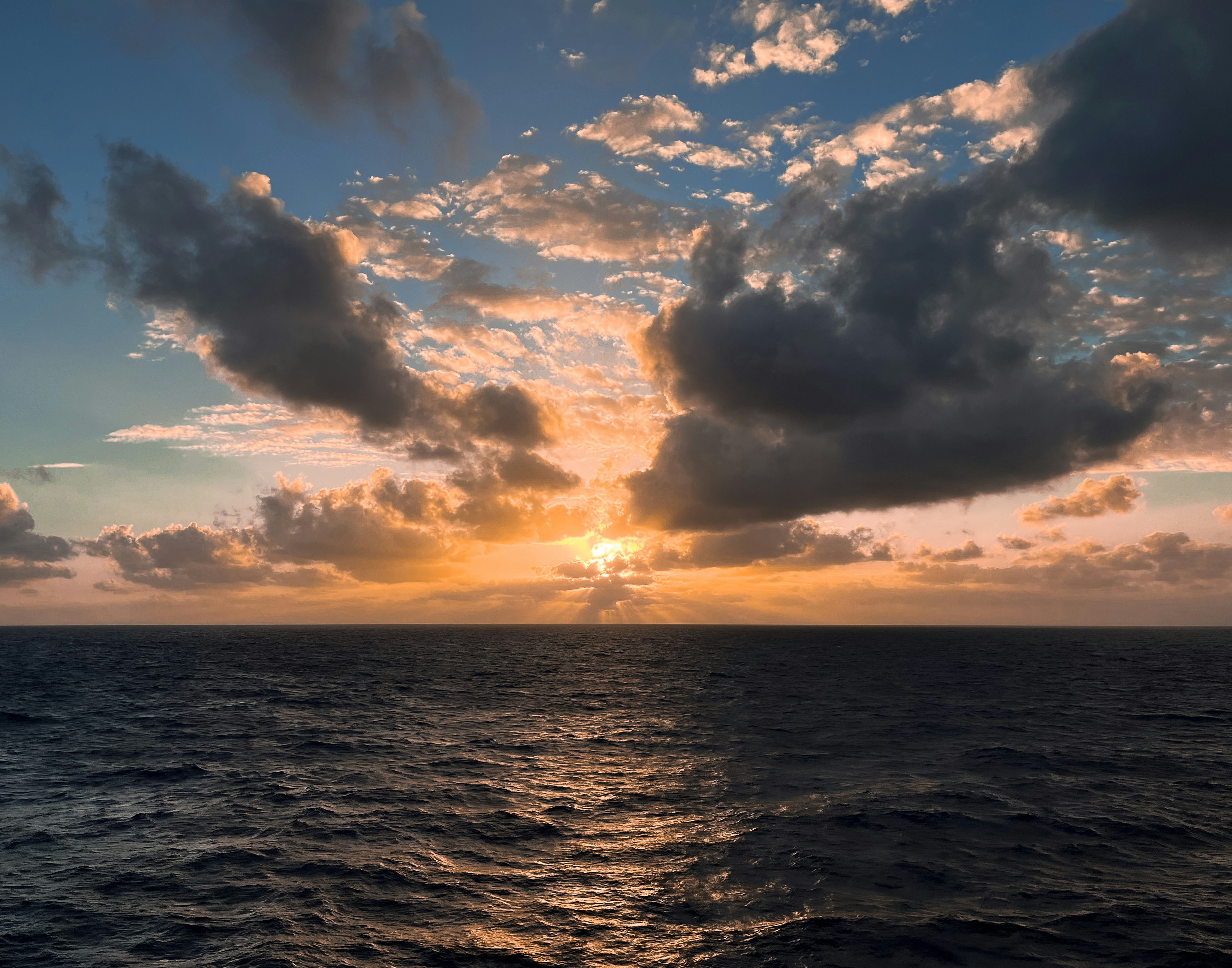 The sun is setting over the ocean on a cloudy day