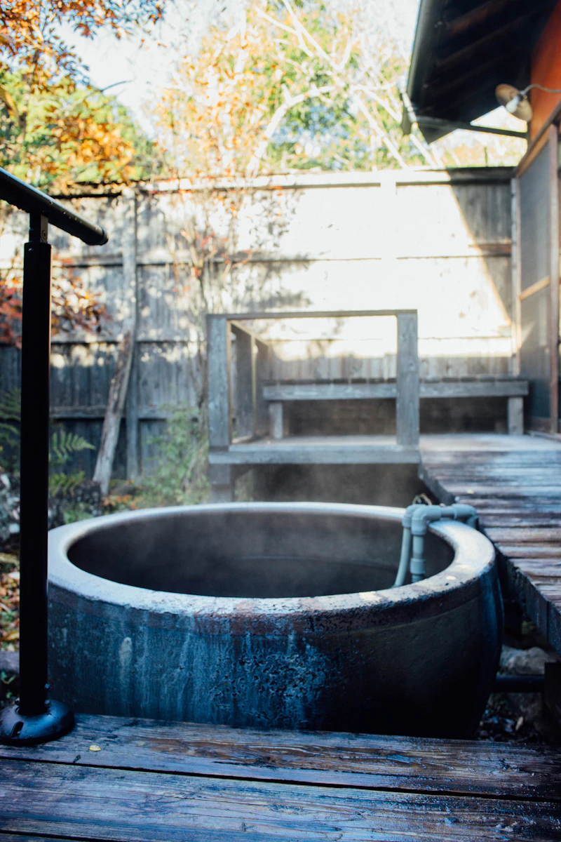 A private wooden outdoor bath tub on a deck overlooking a forested hillside at a Kumamoto ryokan — a rotenburo for exclusive use
