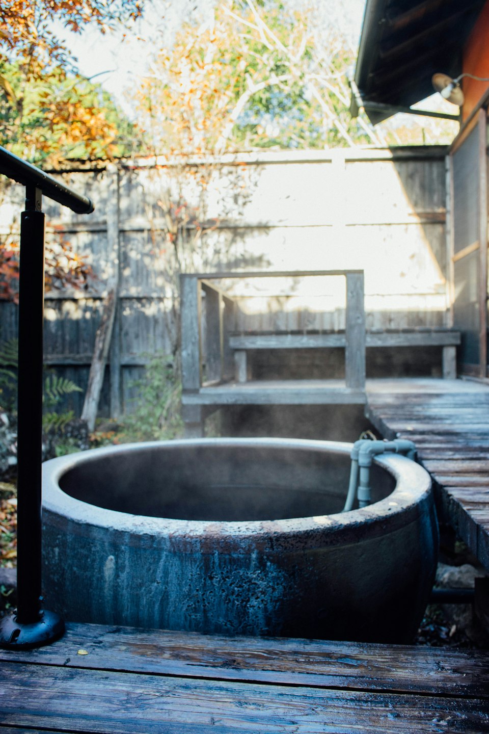 A steaming stone onsen tub on a wooden ryokan deck surrounded by autumn foliage