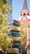 A tower of books in front of a building with a clock