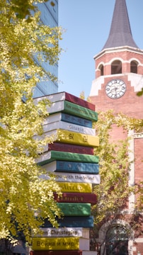 A tower of books in front of a building with a clock