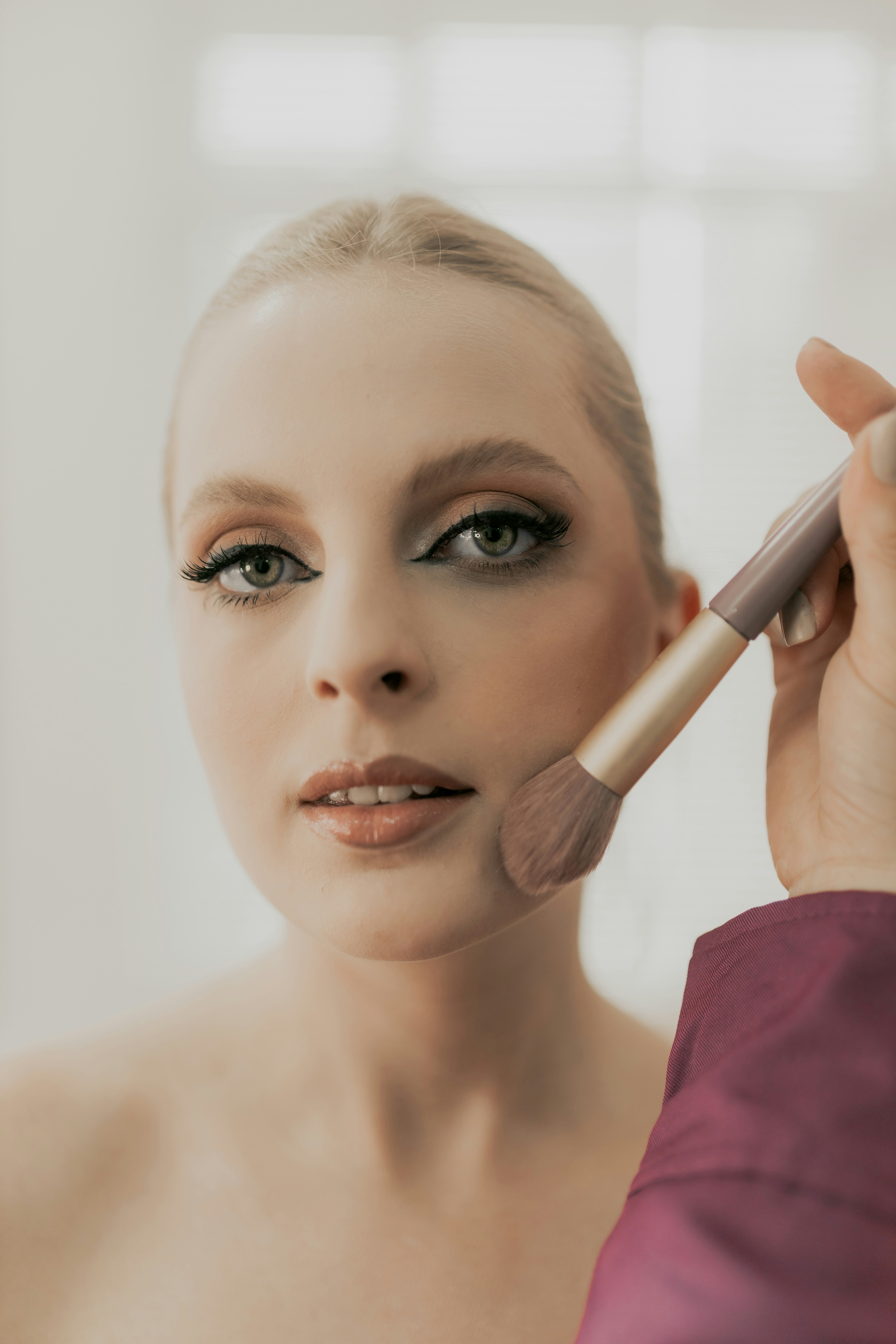 A woman is putting on a makeup brush
