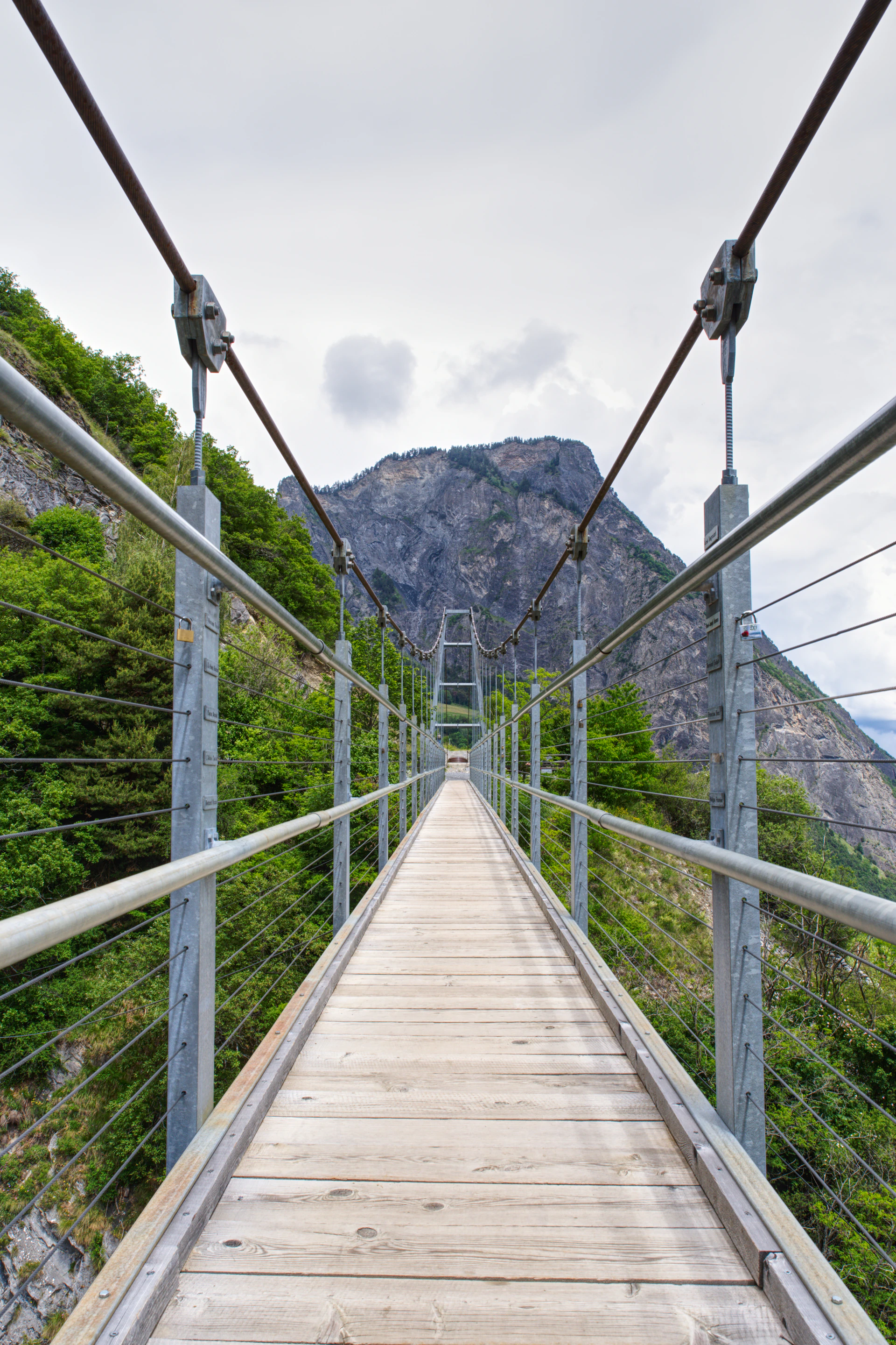 A wooden suspension bridge over a river with mountains in the background