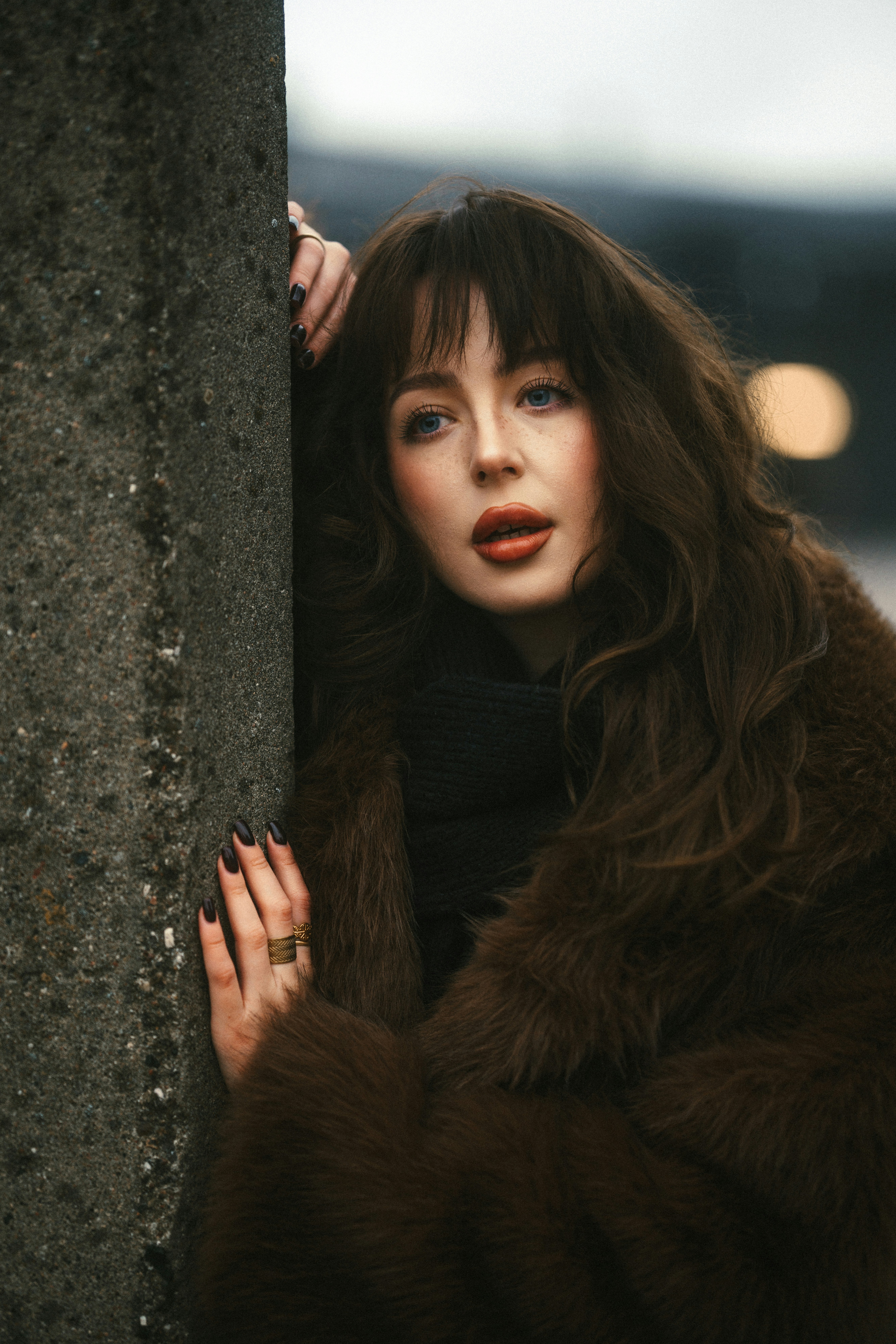 A woman in a fur coat leaning against a wall