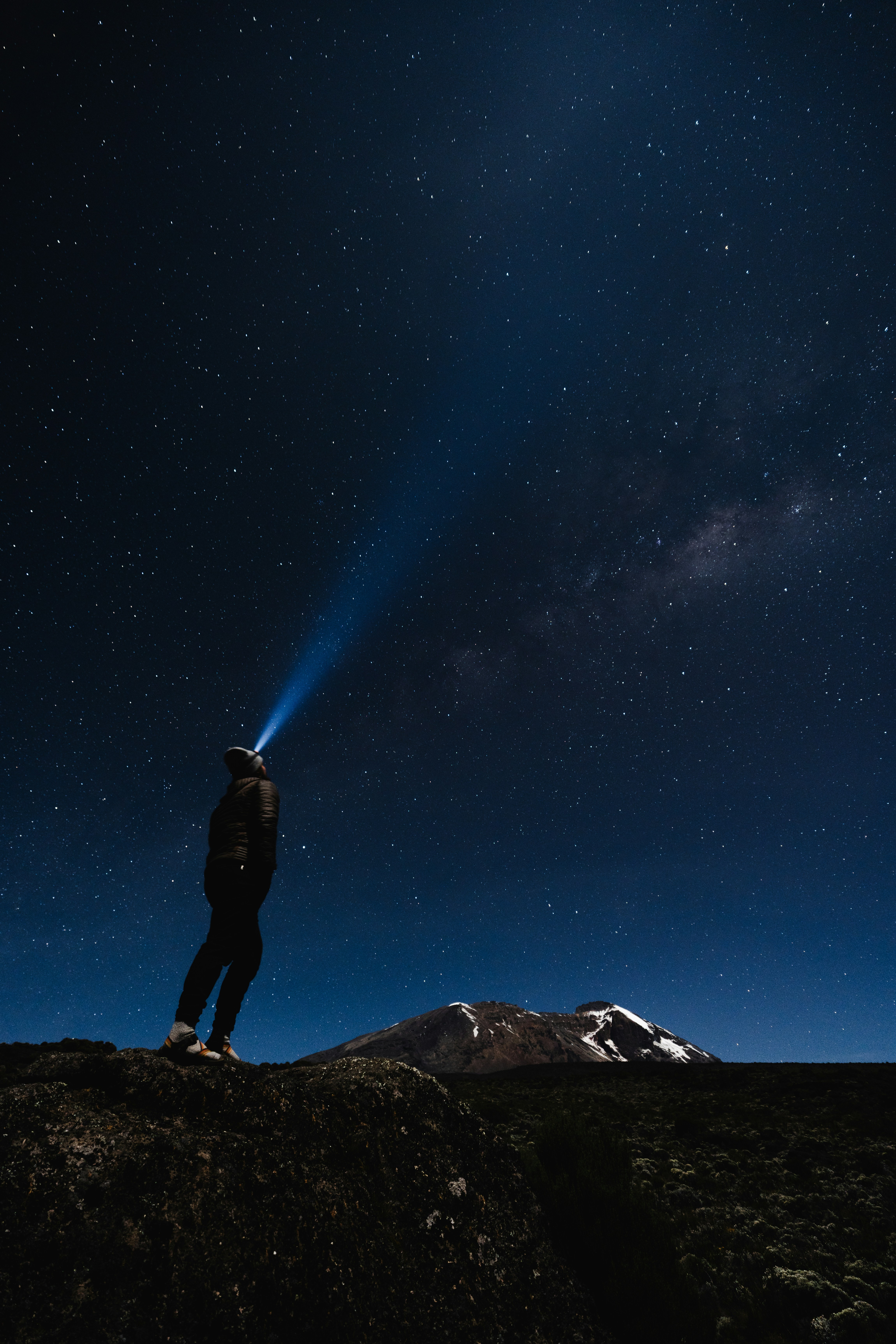 Un hombre de pie en la cima de una montaña bajo un cielo nocturno