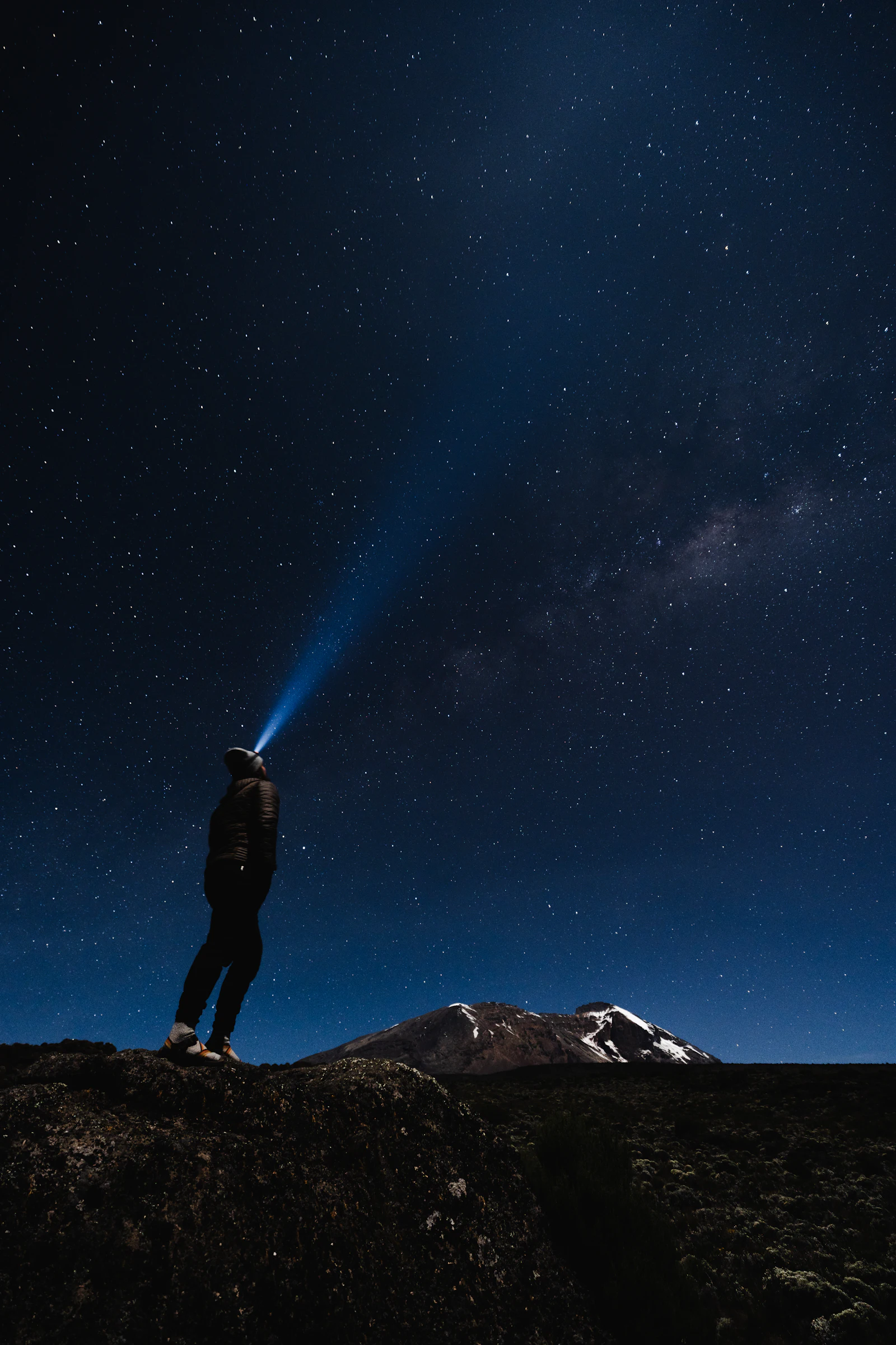 A climber standing under a star-filled night sky on Mount Kilimanjaro