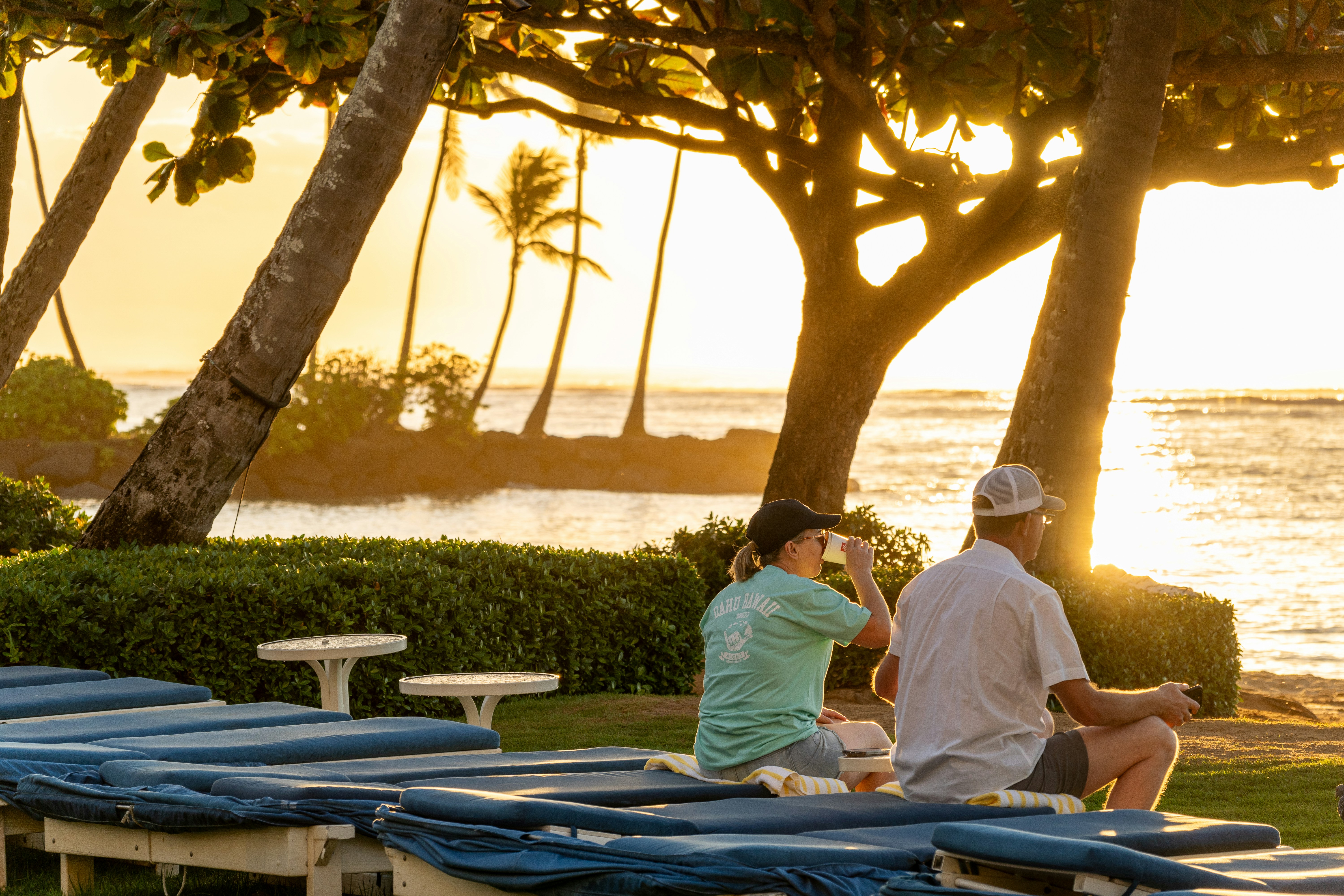 Couple relaxing on sun loungers at beach club, ocean in background, golden afternoon light