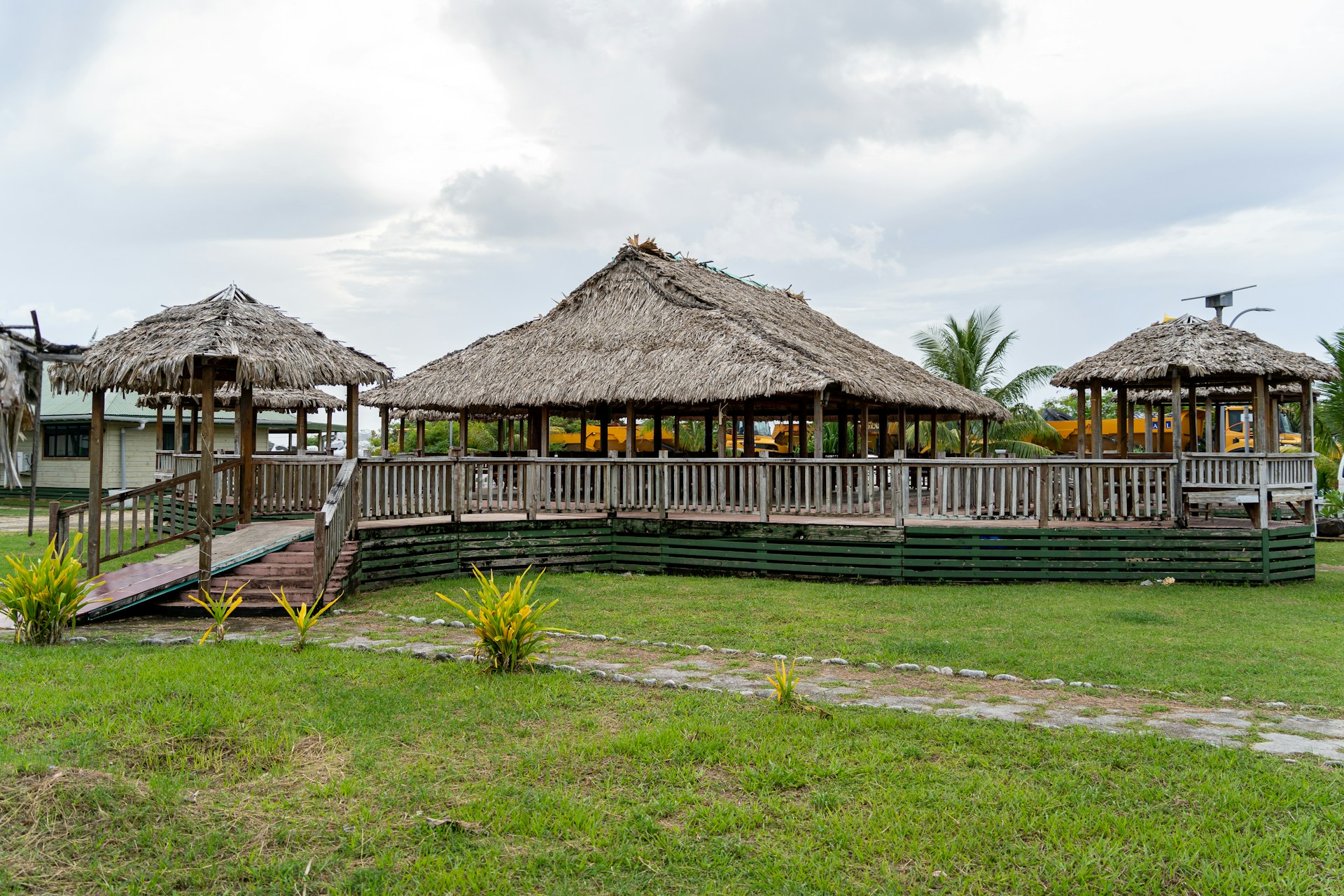A grassy area with a wooden walkway and thatched huts