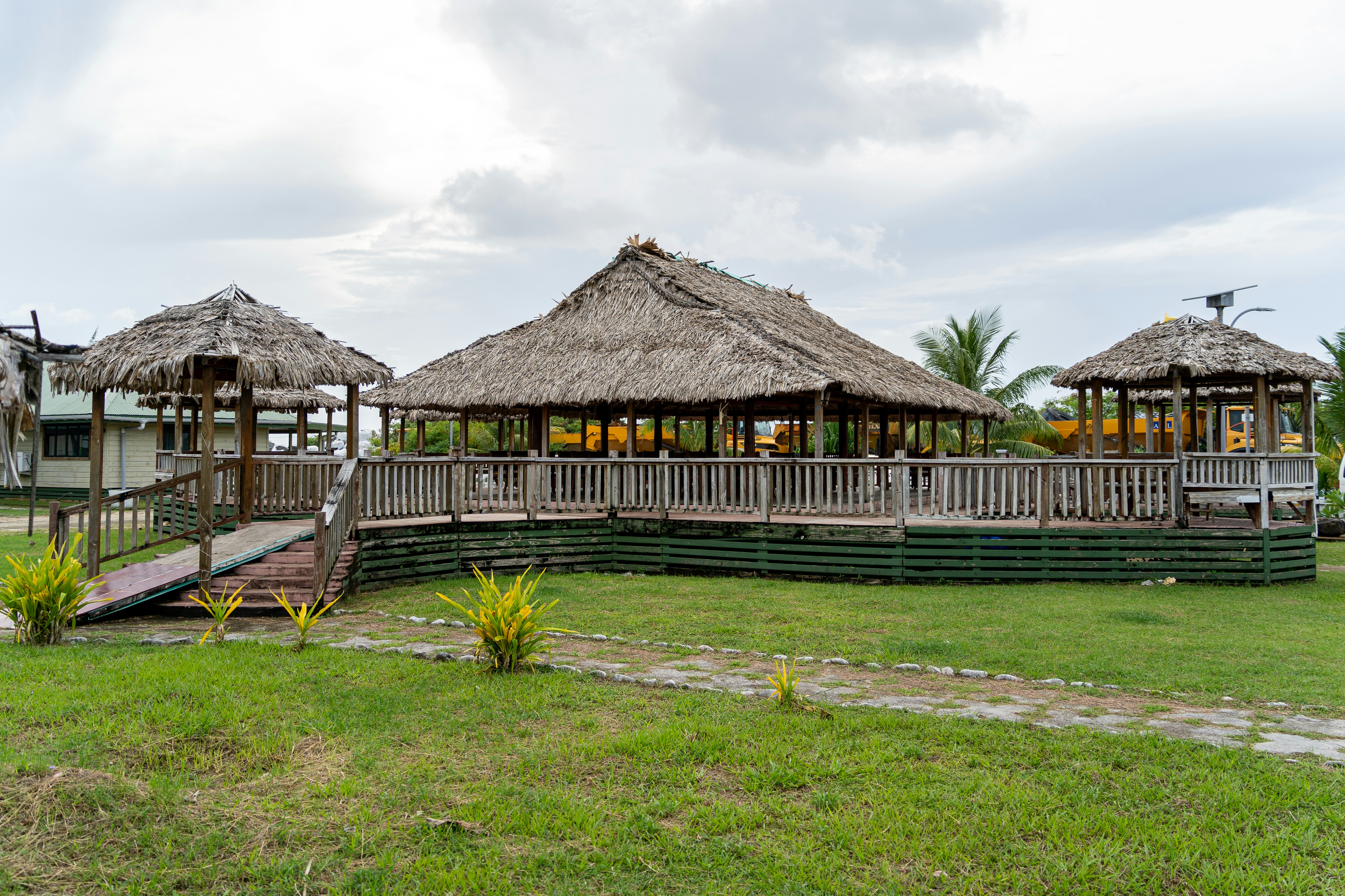 A grassy area with a wooden walkway and thatched huts