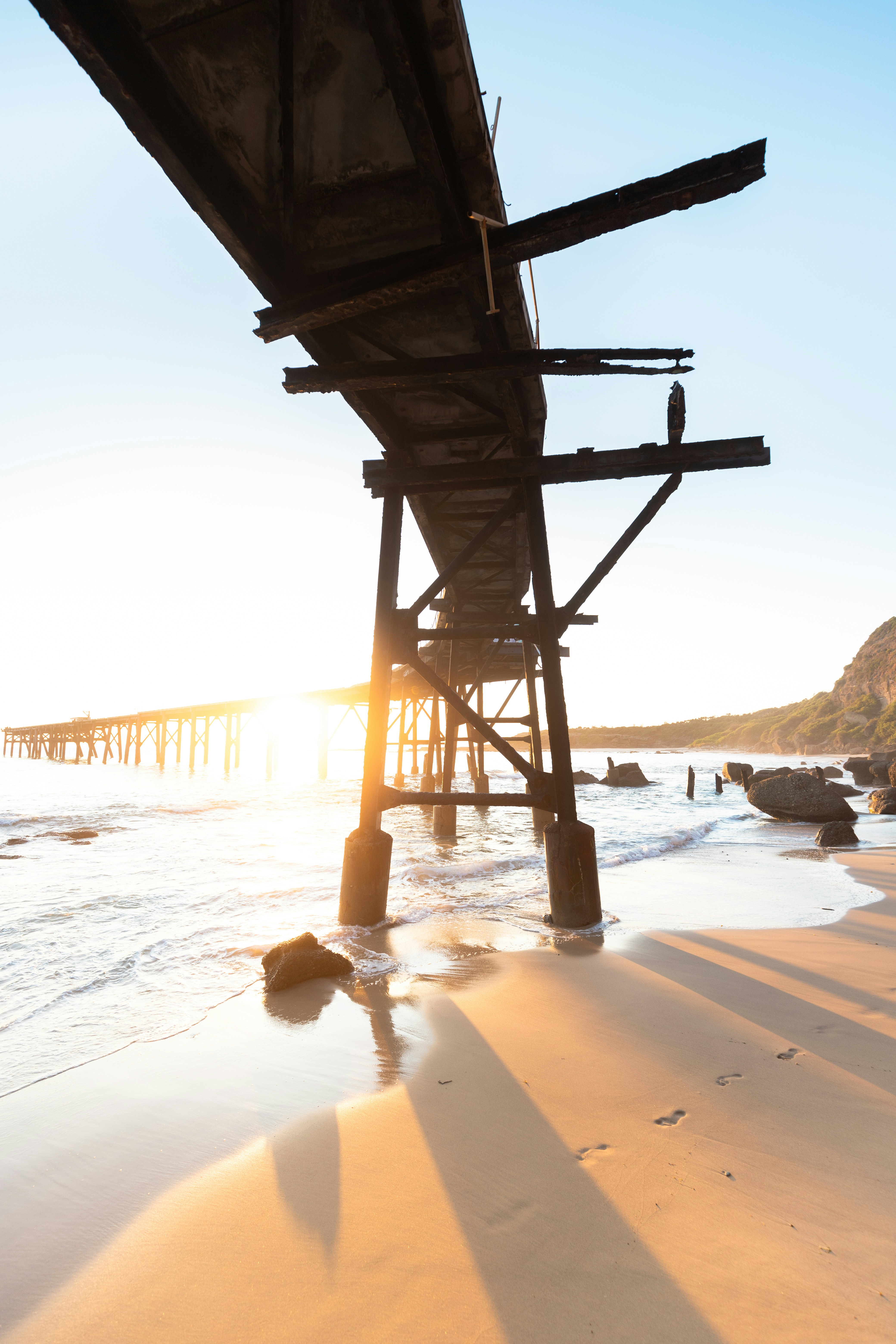 The sun is shining on the beach under a pier