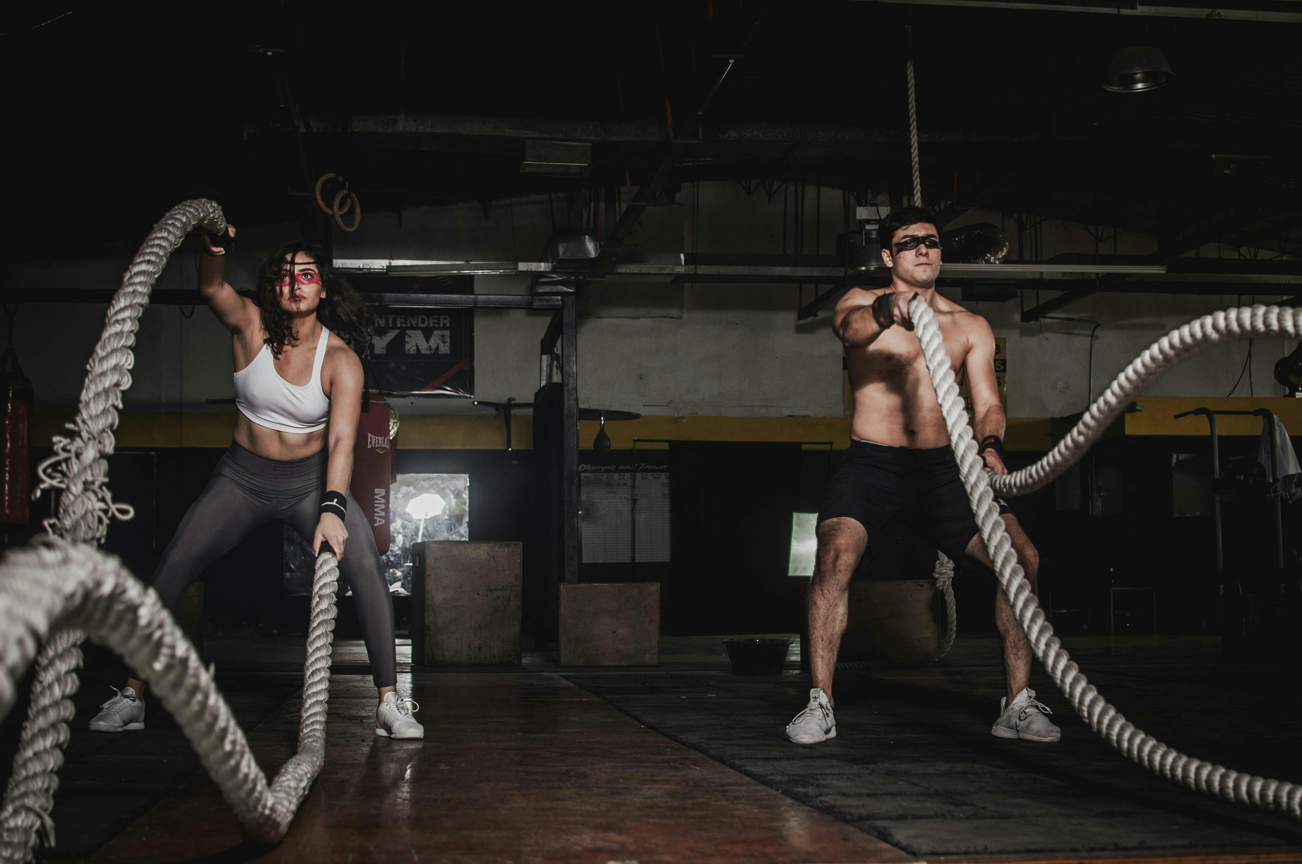 Athlete in battle rope training session, intense effort, dark industrial gym