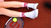 A woman laying on the ground with a tennis racket and ball