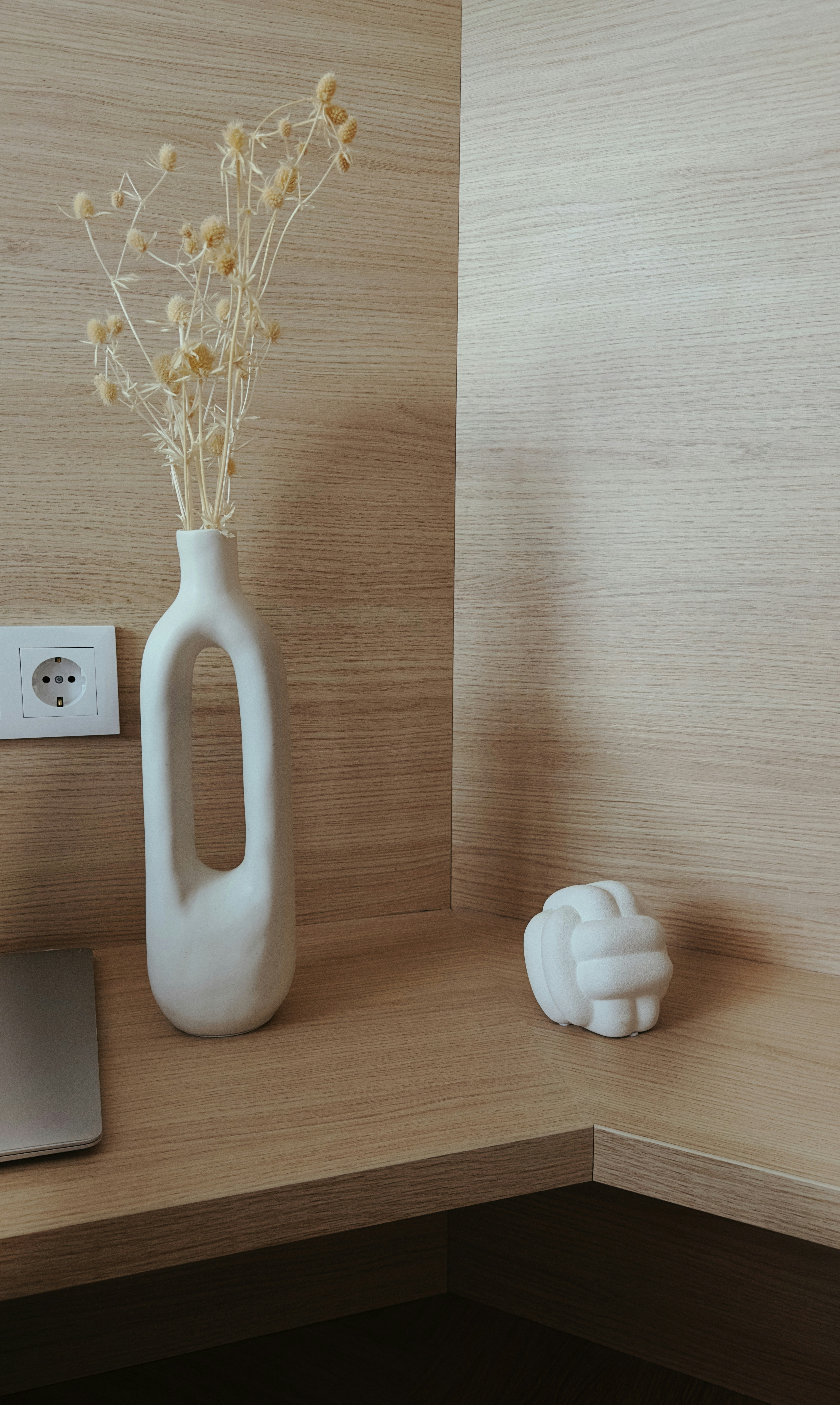 A white vase with flowers in it sitting on a desk