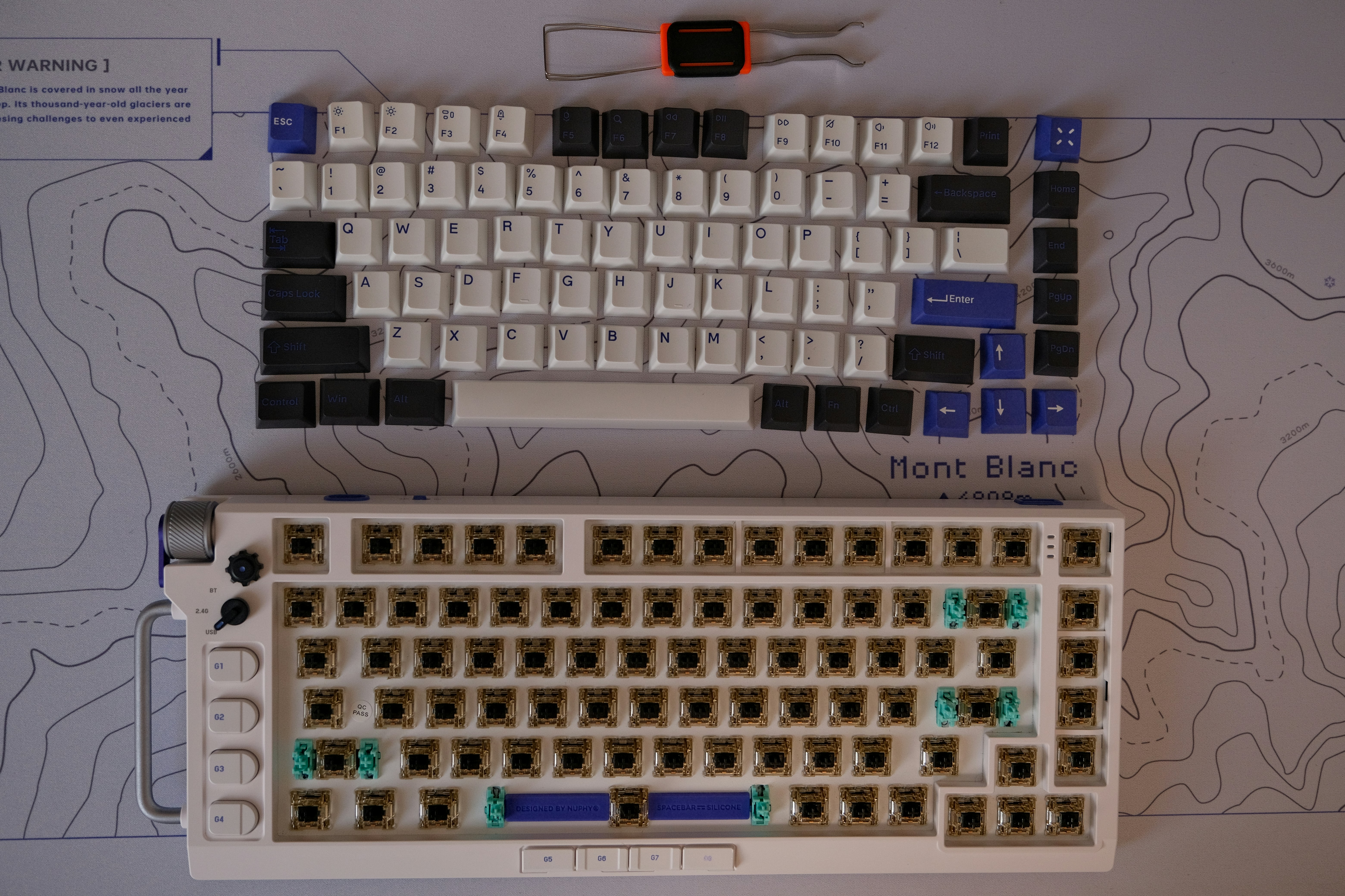 White and blue keyboard dissasembled on top of a white mousepad with blue topographic lines.