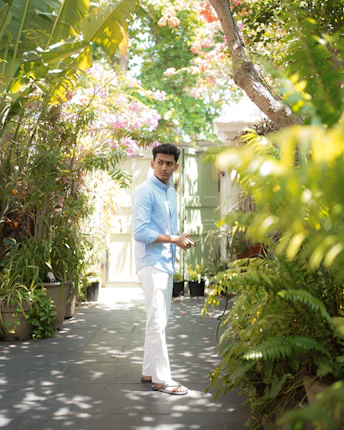 A man in a blue shirt and white pants standing in a garden