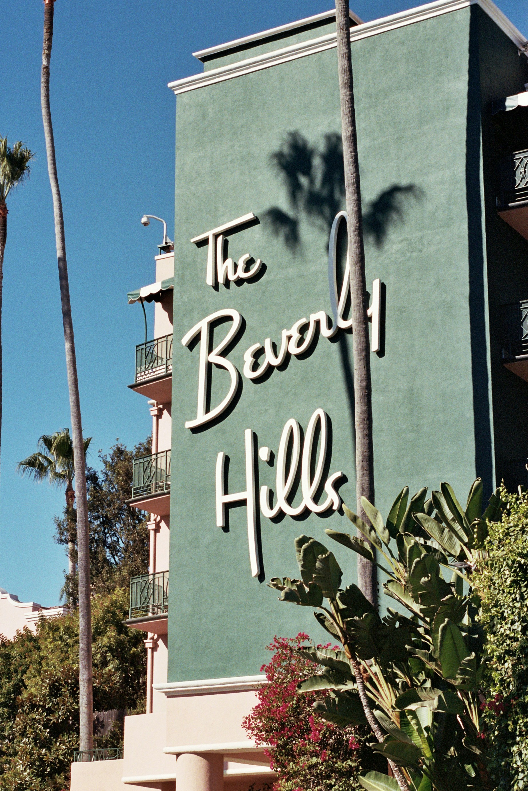 A sign for the beverly hills hotel with palm trees in the background