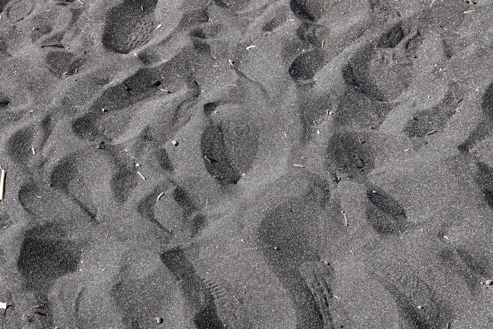 Close-up view of a sandy beach with dark gray sand and scattered small rocks