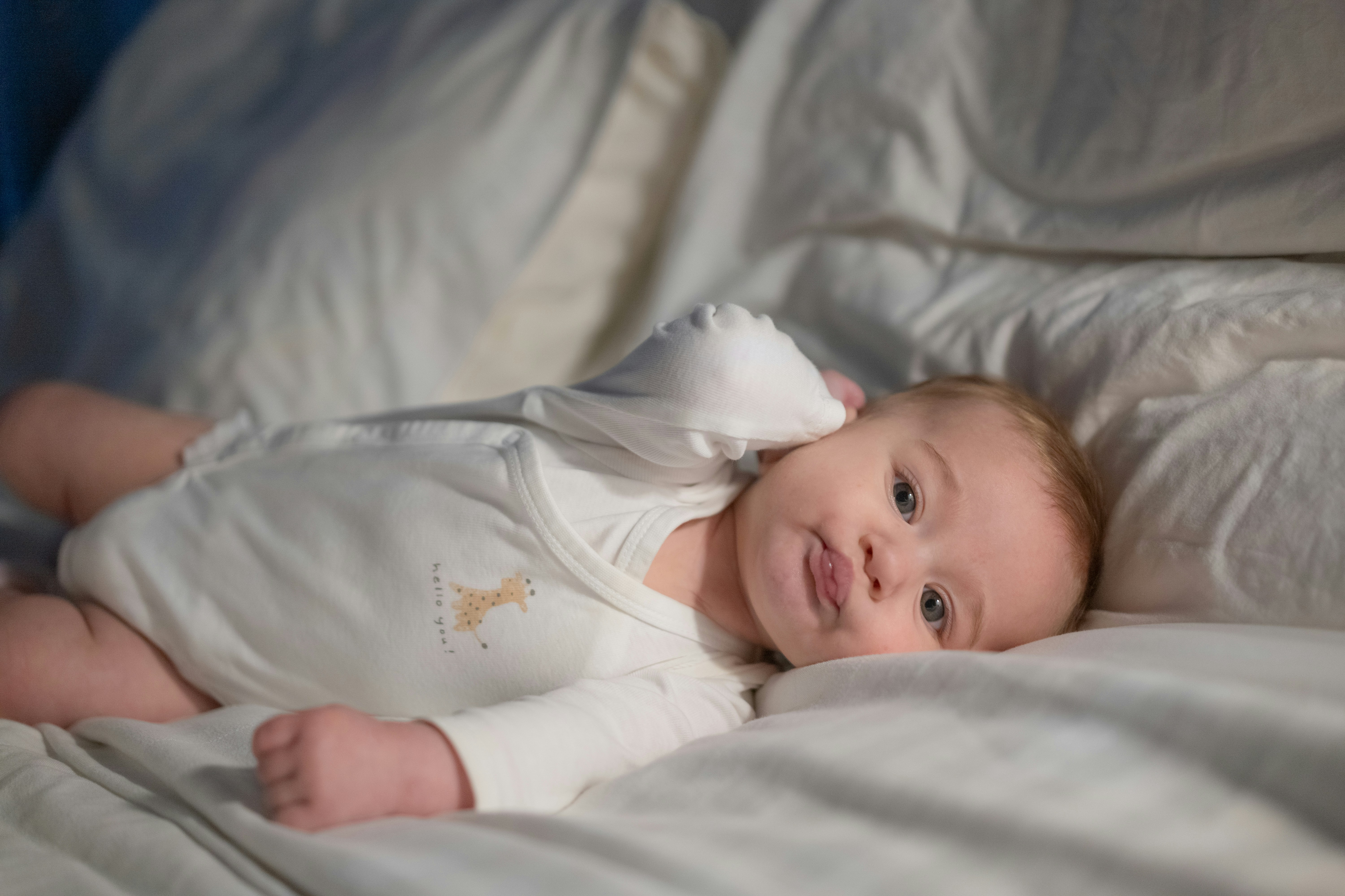 A baby laying on a bed with white sheets
