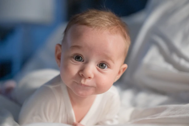 A baby laying on a bed with white sheets