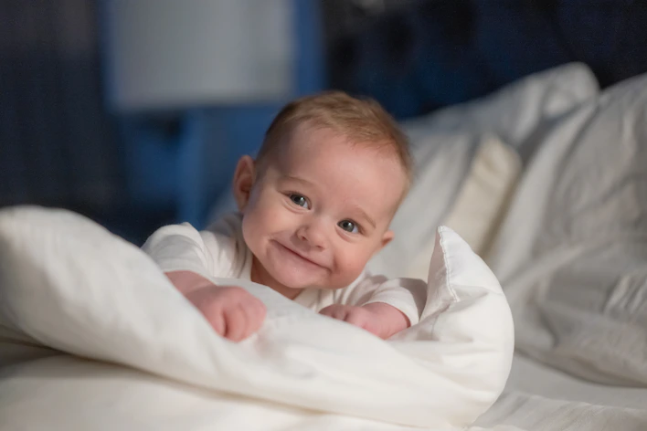 A smiling baby wrapped in a blanket on a bed