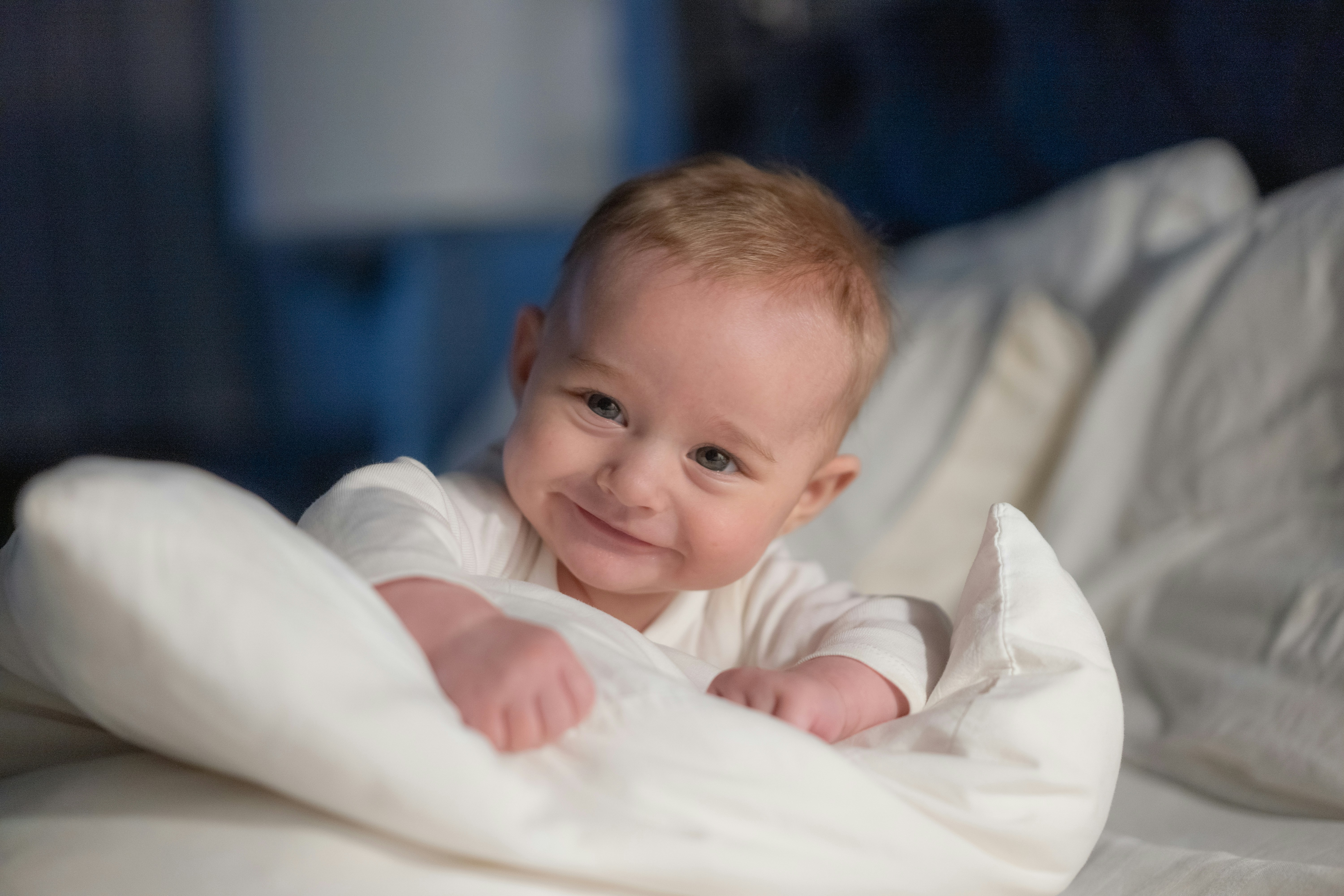 A baby laying on a bed with a white blanket