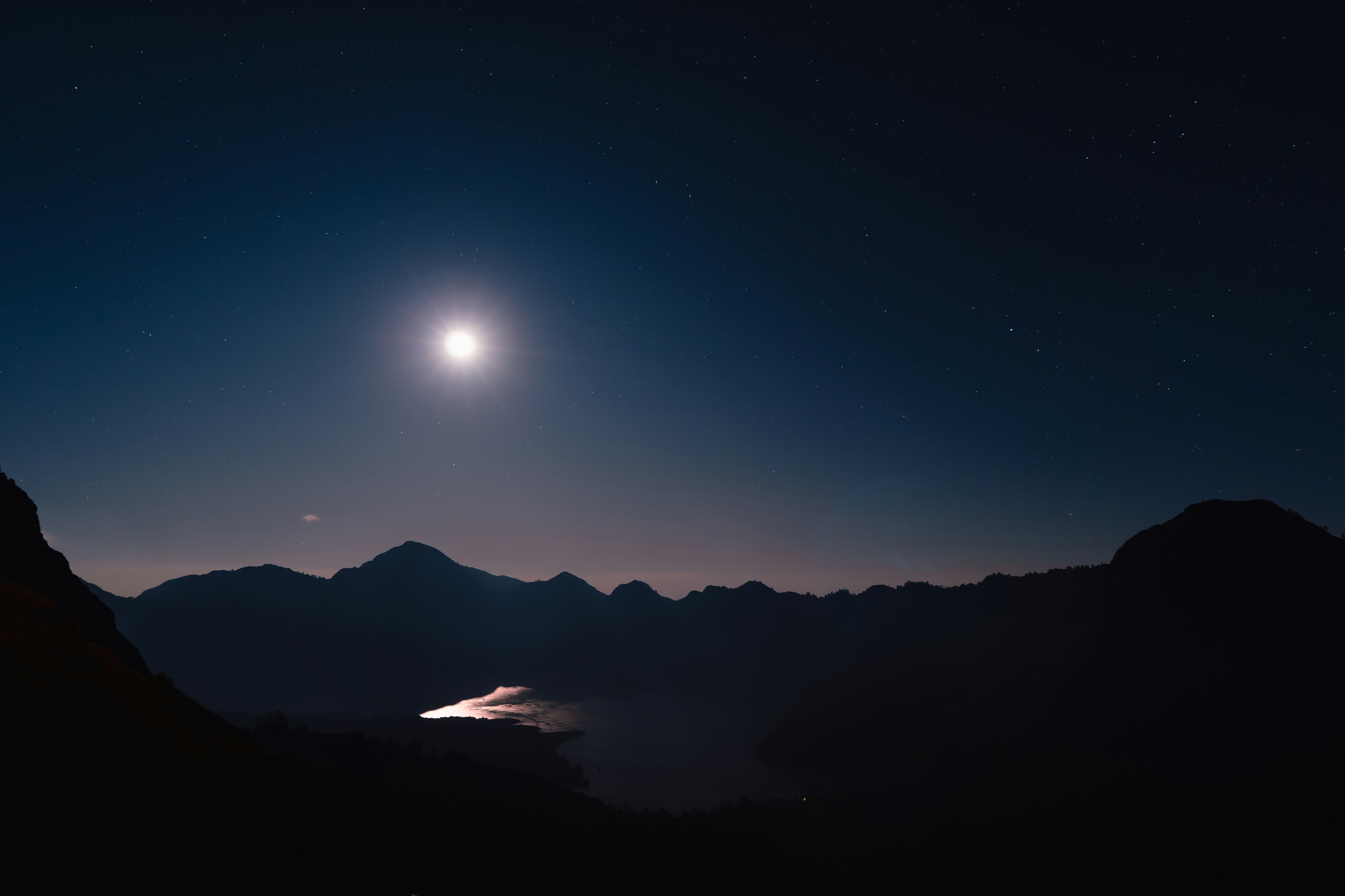 A view of a mountain at night with the moon in the sky