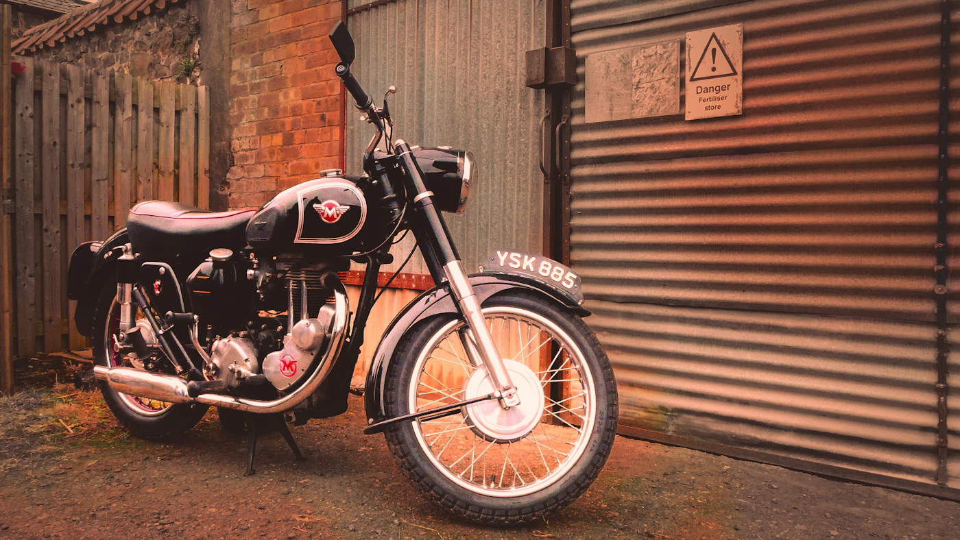 Vintage motorcycle with orange spoked wheels against a brick wall