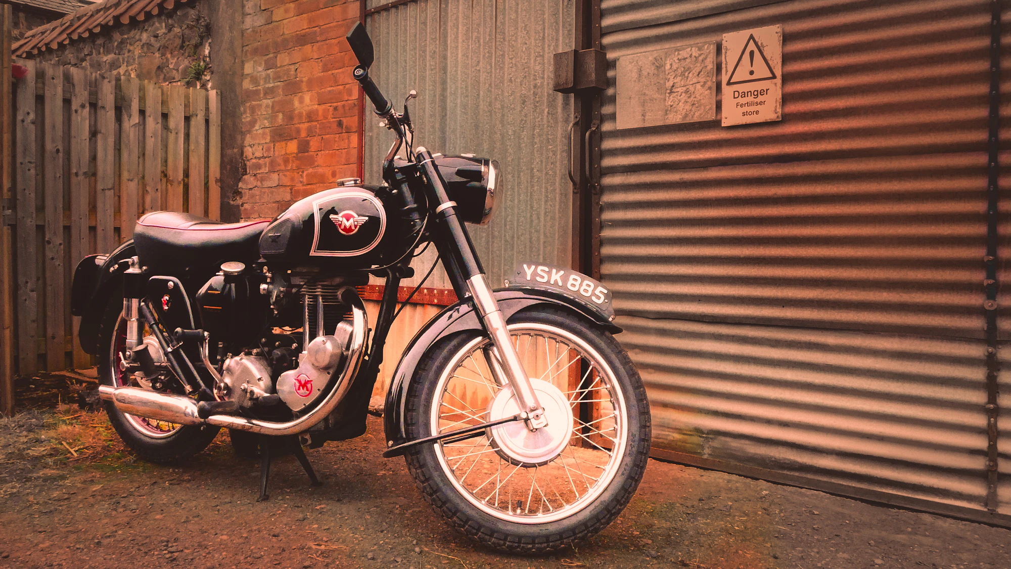 Vintage motorcycle with orange spoked wheels against a brick wall