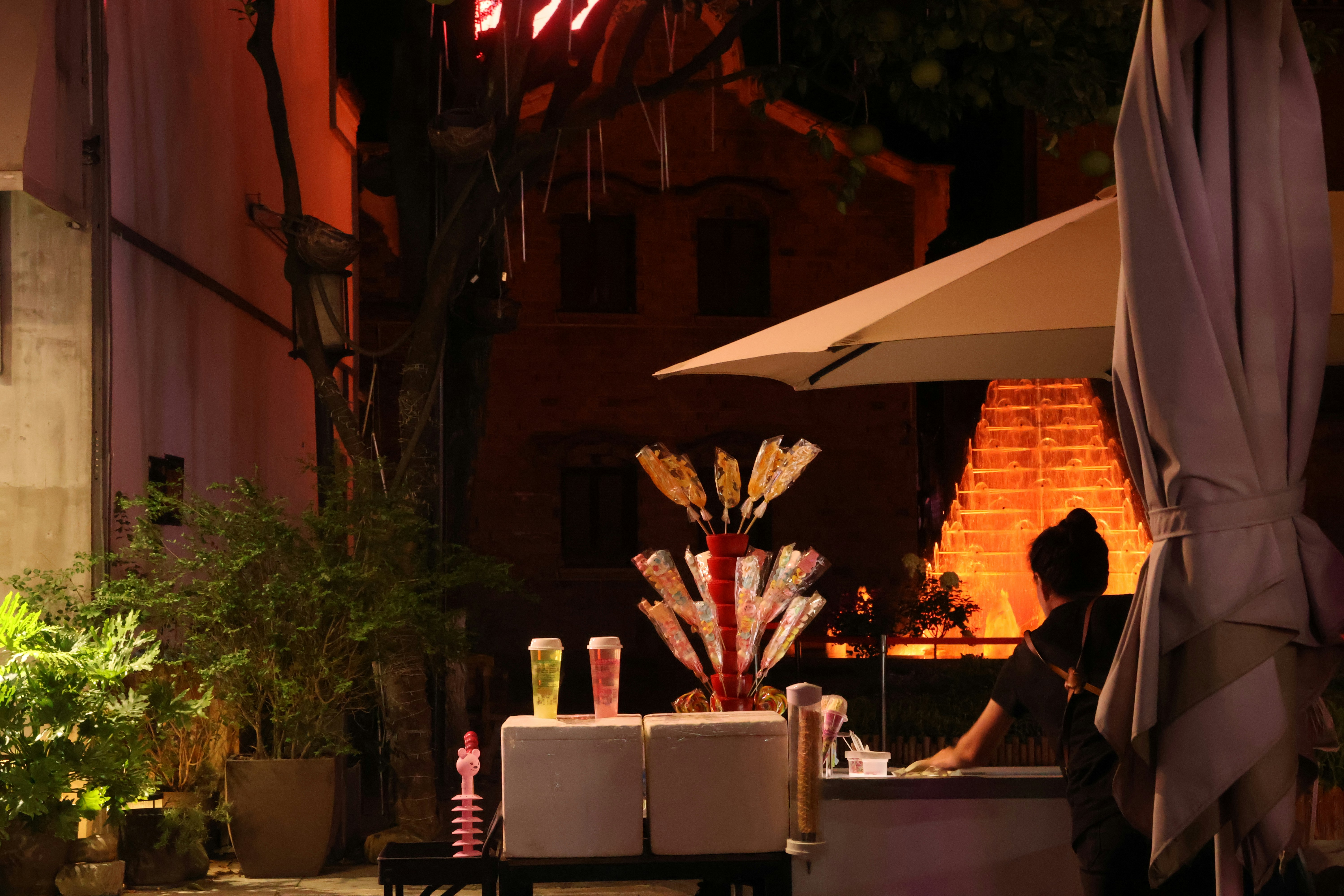 a vendor is preparing her sweets booth as the street is getting busy in the night.